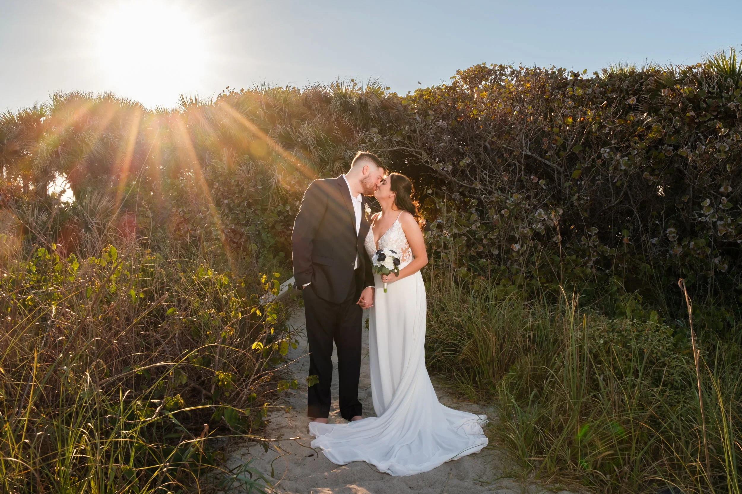Bride and groom kissing on the sand at Cocoa Beach with a sunburst as the sun starts to set. Photo taken by Dawn Aiello Photography.