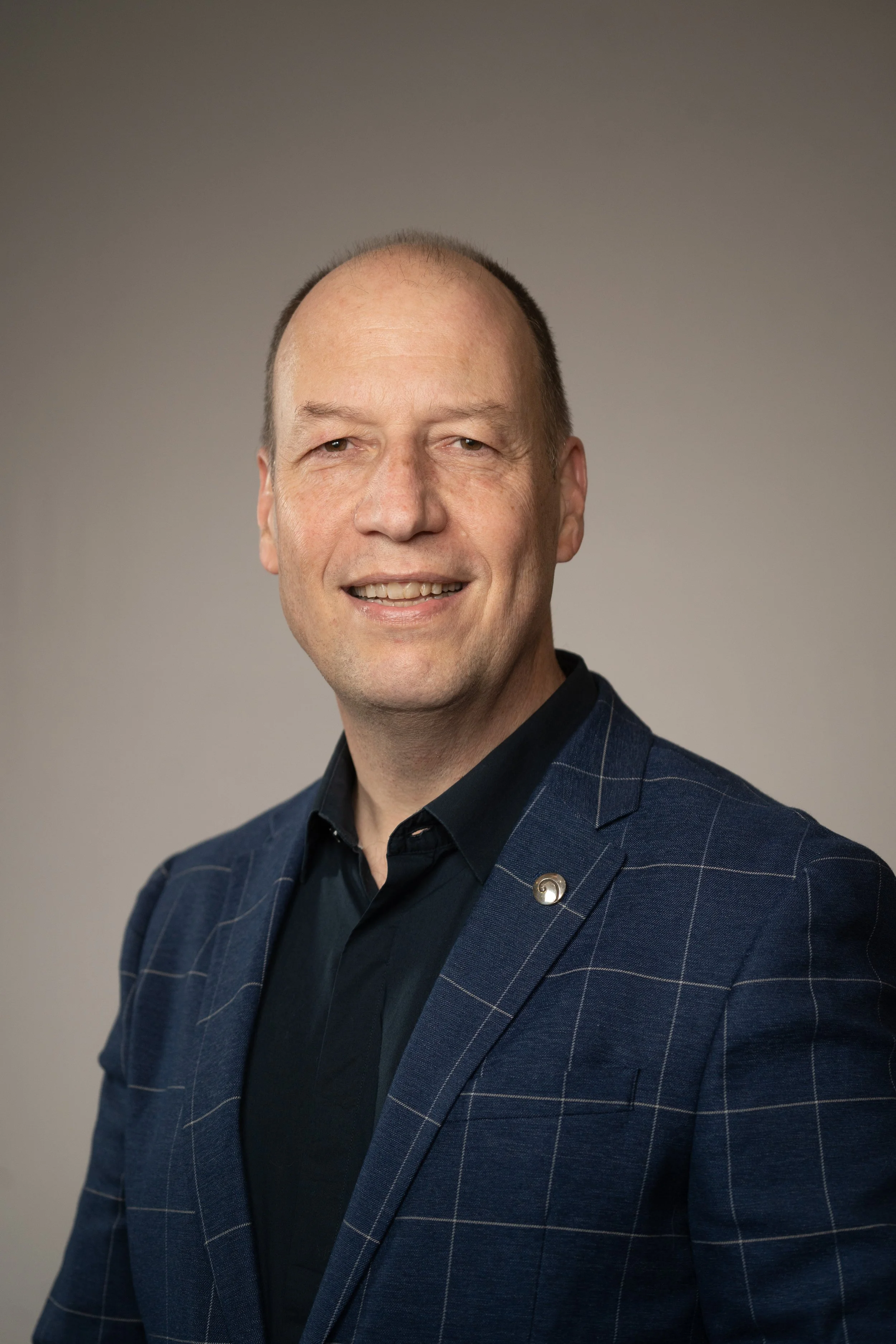 Photograph of Michael Warszawski in a navy blue sport jacket with a silver pin and dark blue shirt. 