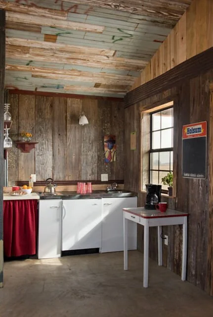 Rustic kitchen with wooden panel walls, a small white table, a window, and vintage-style decor.