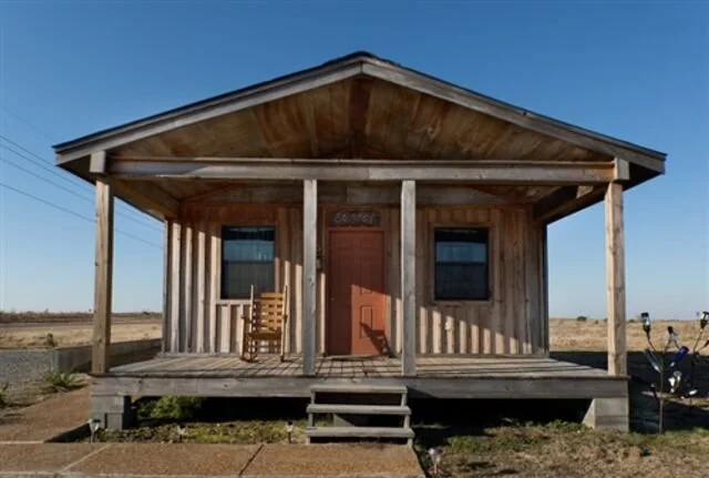 A small wooden building with a front porch, two windows, and a door labeled "Business" on a clear day with a blue sky.