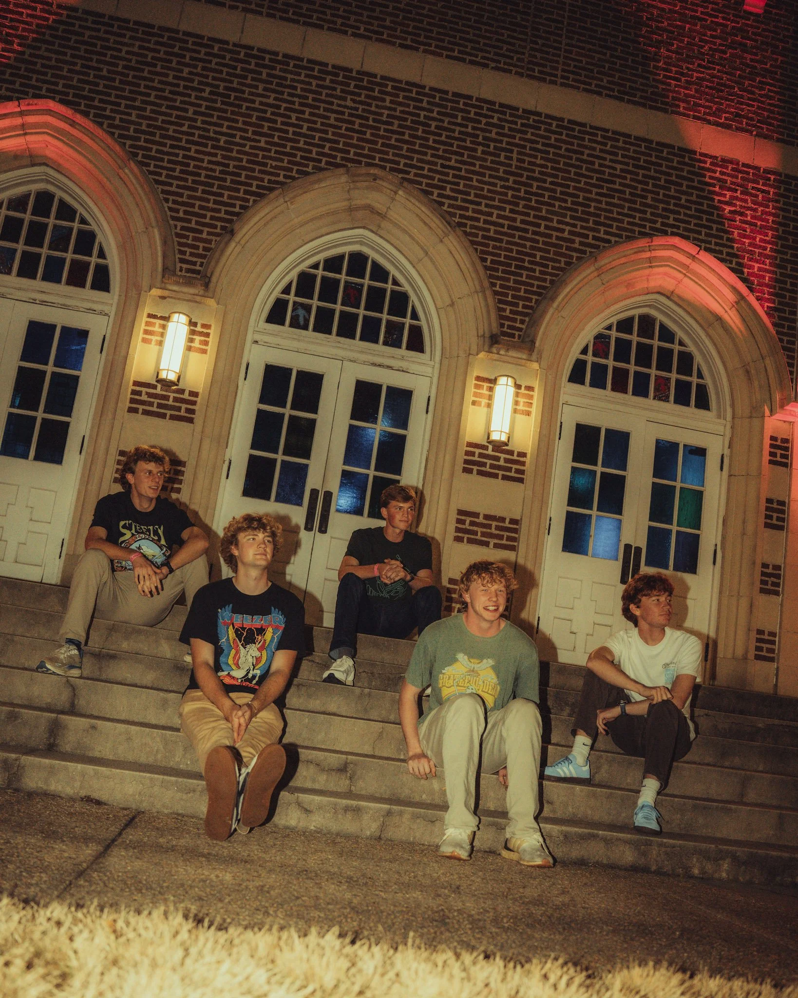 Four young friends standing together outdoors at night, smiling and enjoying each other's company.