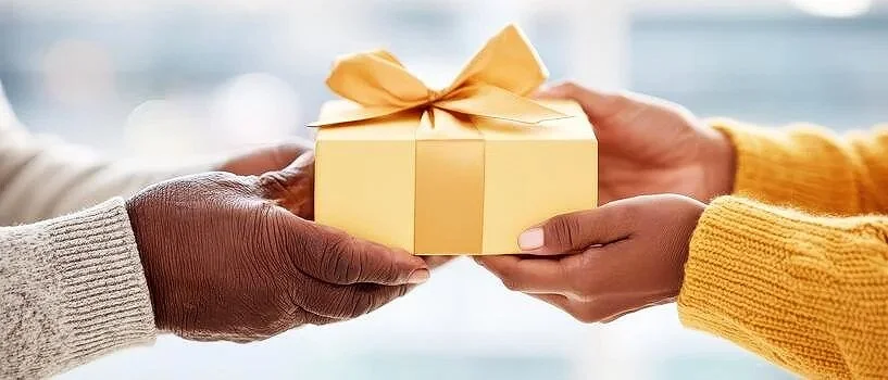 Hands exchanging a wrapped corporate gift box tied with gold ribbon
