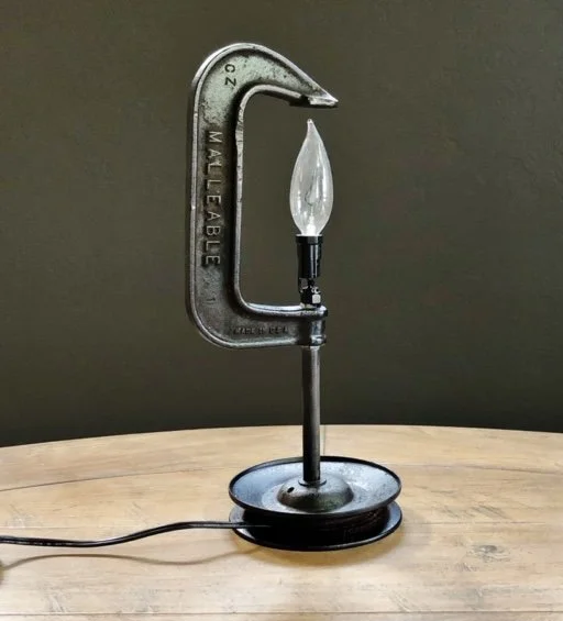 A lamp made from a large metal C-clamp with a light bulb attached to the top, placed on a wooden surface.