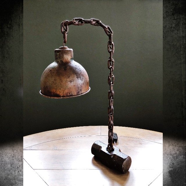 A vintage industrial desk lamp with a rusted metal shade, attached to a chain and mounted on a wooden surface.