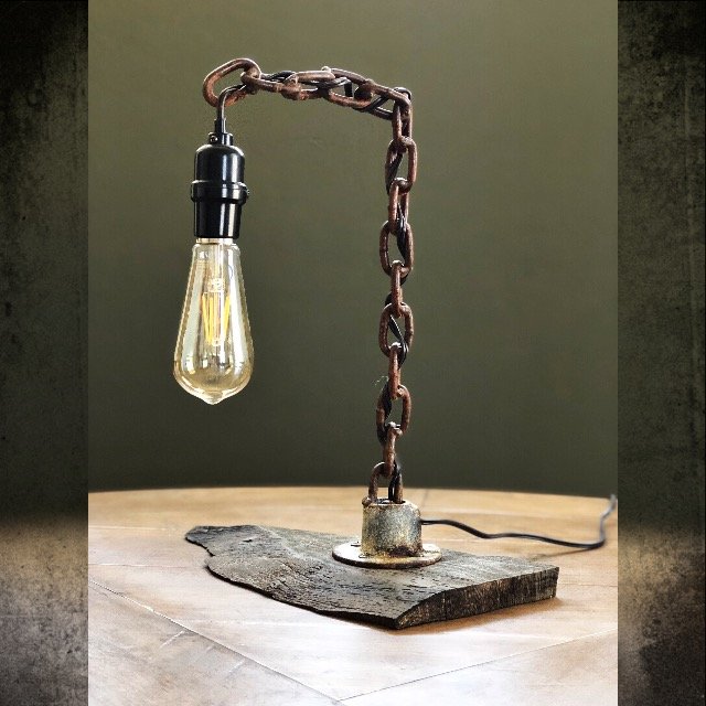 A unique desk lamp made from a lightbulb, a metal chain, and a wooden base with an electrical cord.
