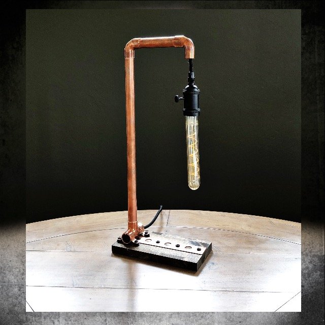 Laboratory setup with copper pipe, black fittings, and a glass test tube with liquid, on a wooden table.