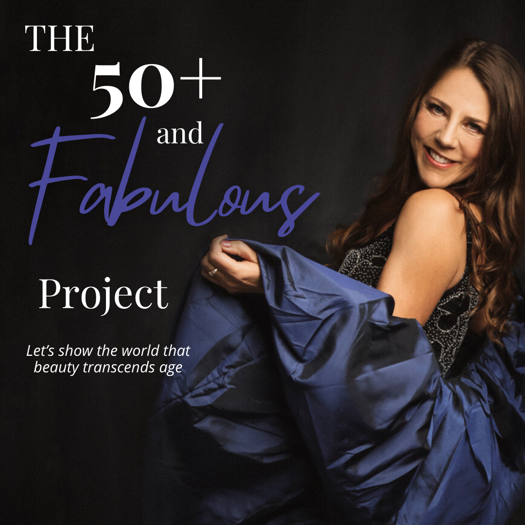 Promotional poster featuring a smiling woman with long brown hair, wearing a black and white outfit and a blue jacket, against a dark background. The poster reads 'The 50+ and Fabulous Project' with a tagline underneath that says 'Let's show the world that beauty transcends age.'