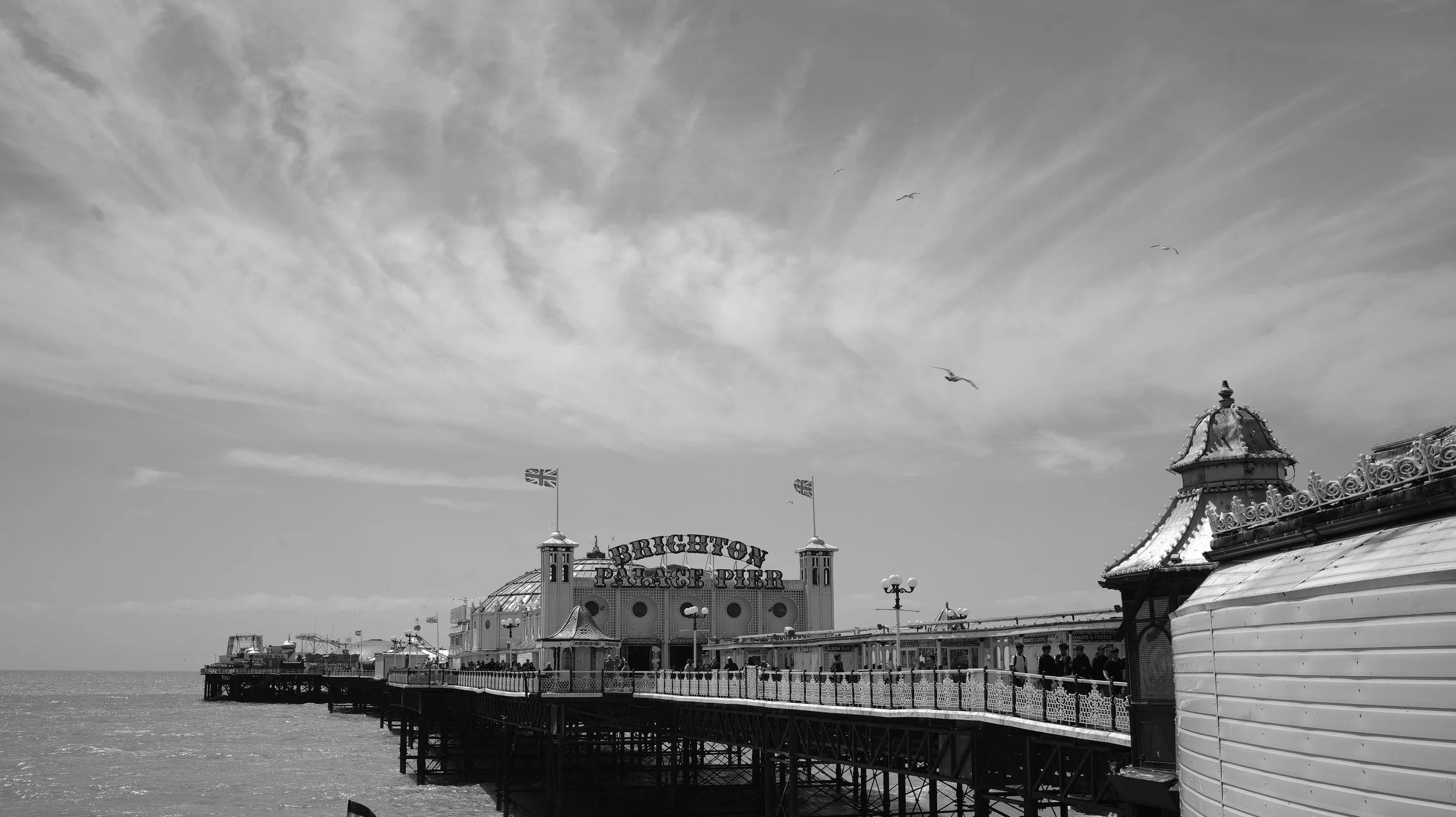 Black and white photo of Brighton Palace Pier with a cloudy sky and seagulls in the air in Brighton, England.