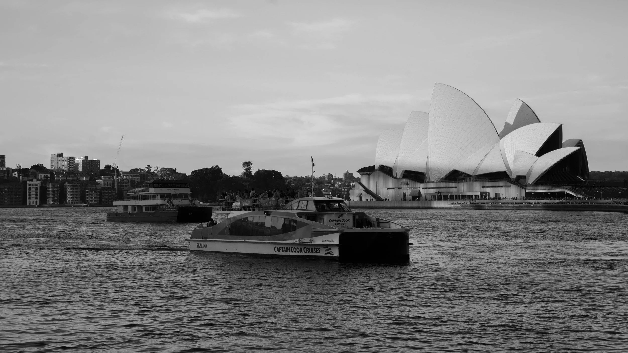 View of boats on a river with the Sydney Opera House in the background, in black and white.