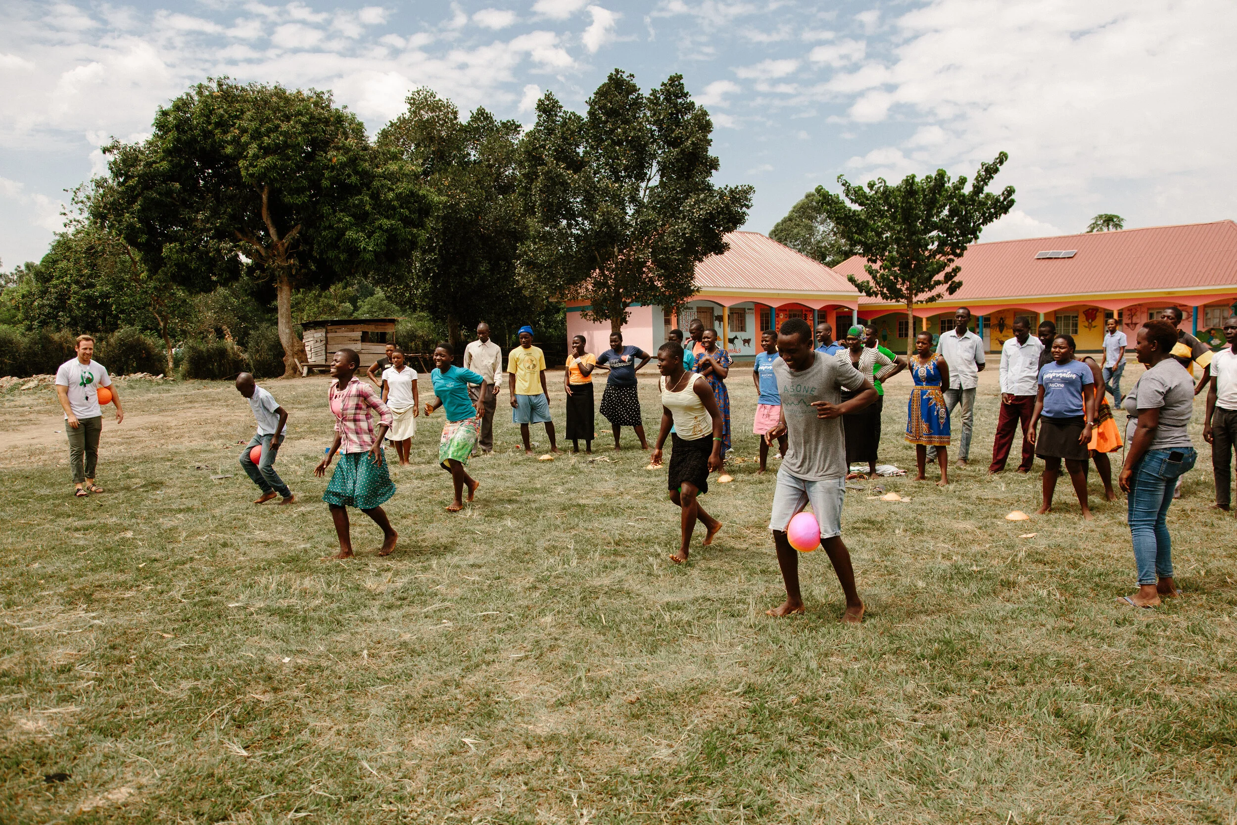 Alt text: "AsOne immersion trip participants playing a ball game with community members on a field near school buildings