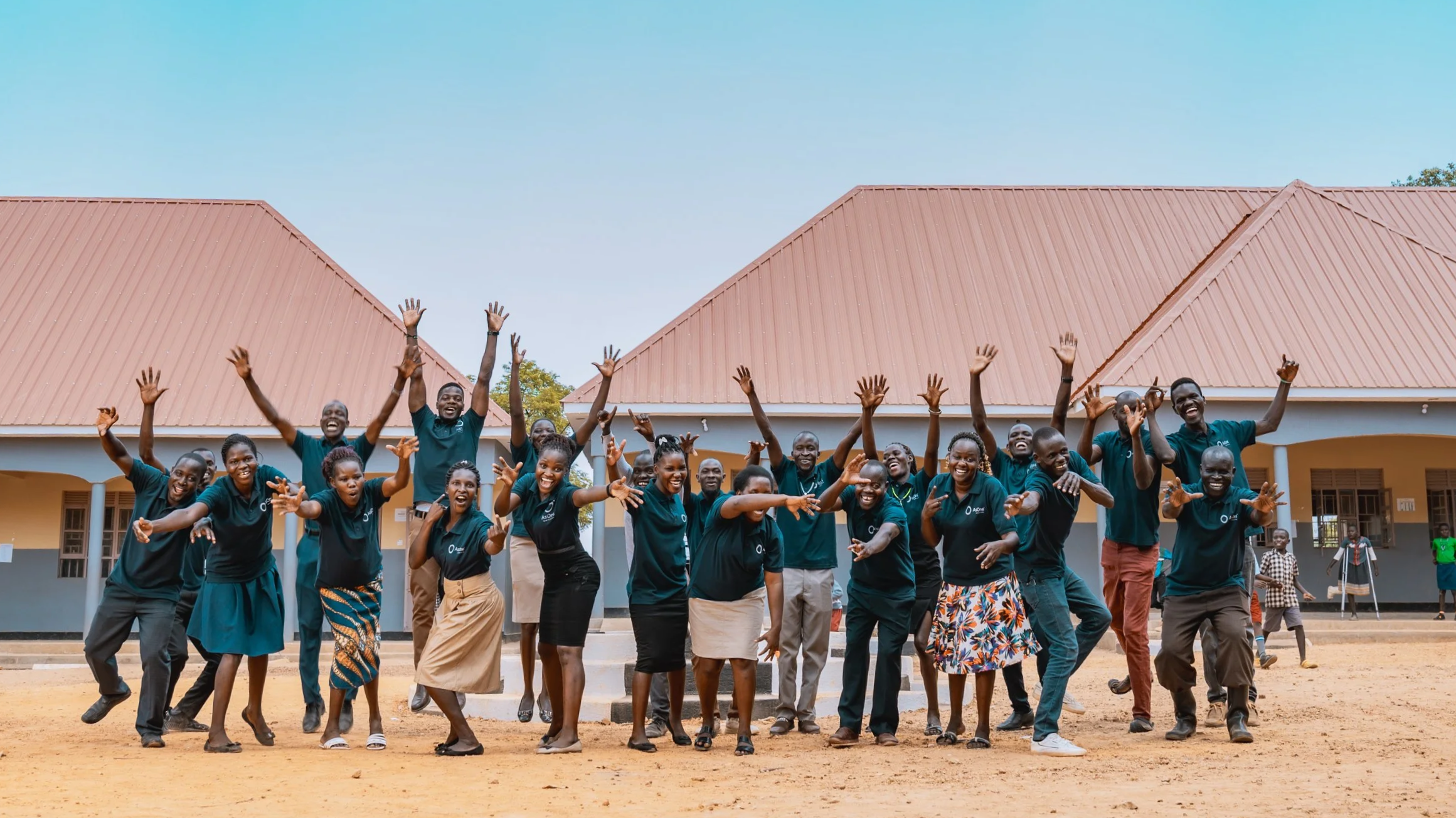 AsOne teachers celebrating with raised hands outside AsOne Nursery & Primary School in Serere, Uganda.