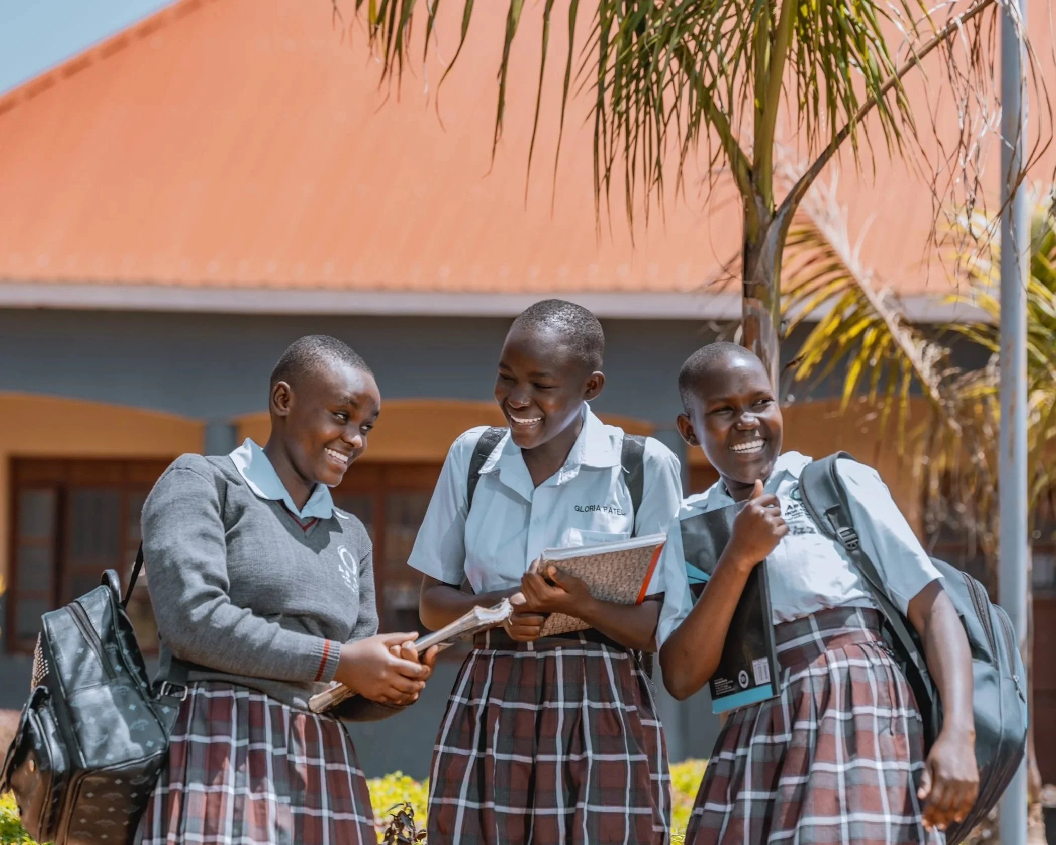 AsOne High School, Pallisa students smiling and chatting together in uniform on campus, carrying backpacks and notebooks