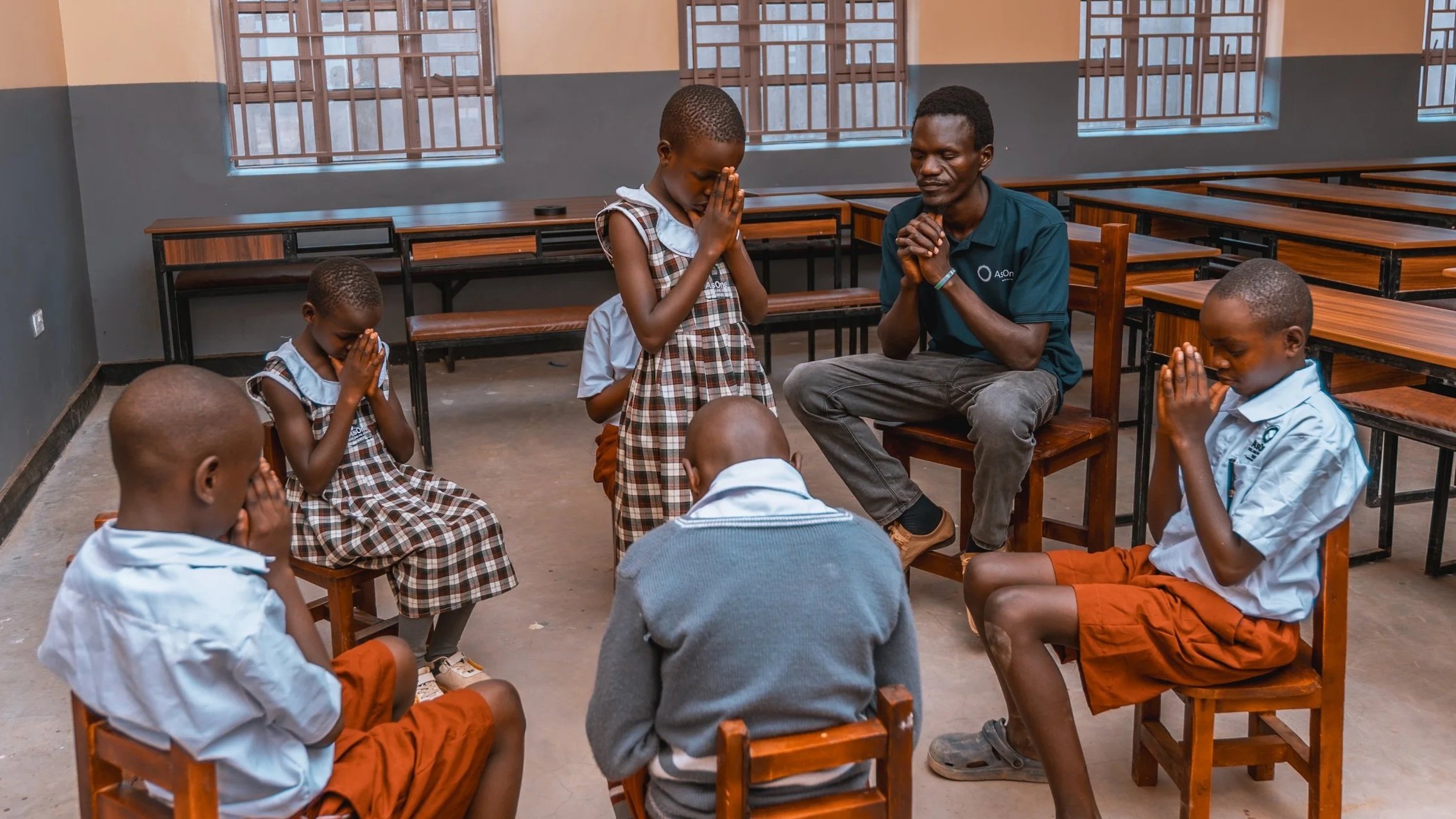 AsOne Nursery & Primary School, Serere students praying in a classroom, led by their teacher