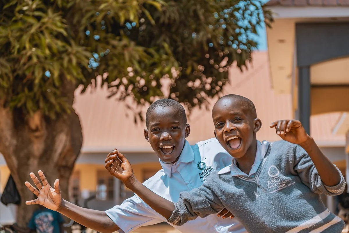 Two laughing AsOne Nursery and Primary School, Serere students in uniform outdoors