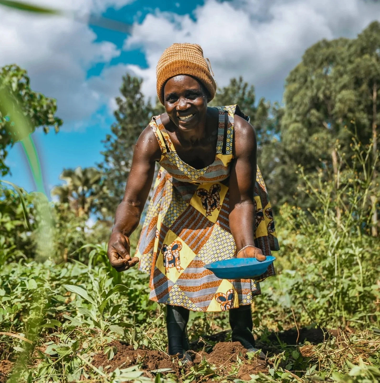 Smiling AsOne farmer harvesting crops into a bowl in a field in Kaberamaido, Uganda