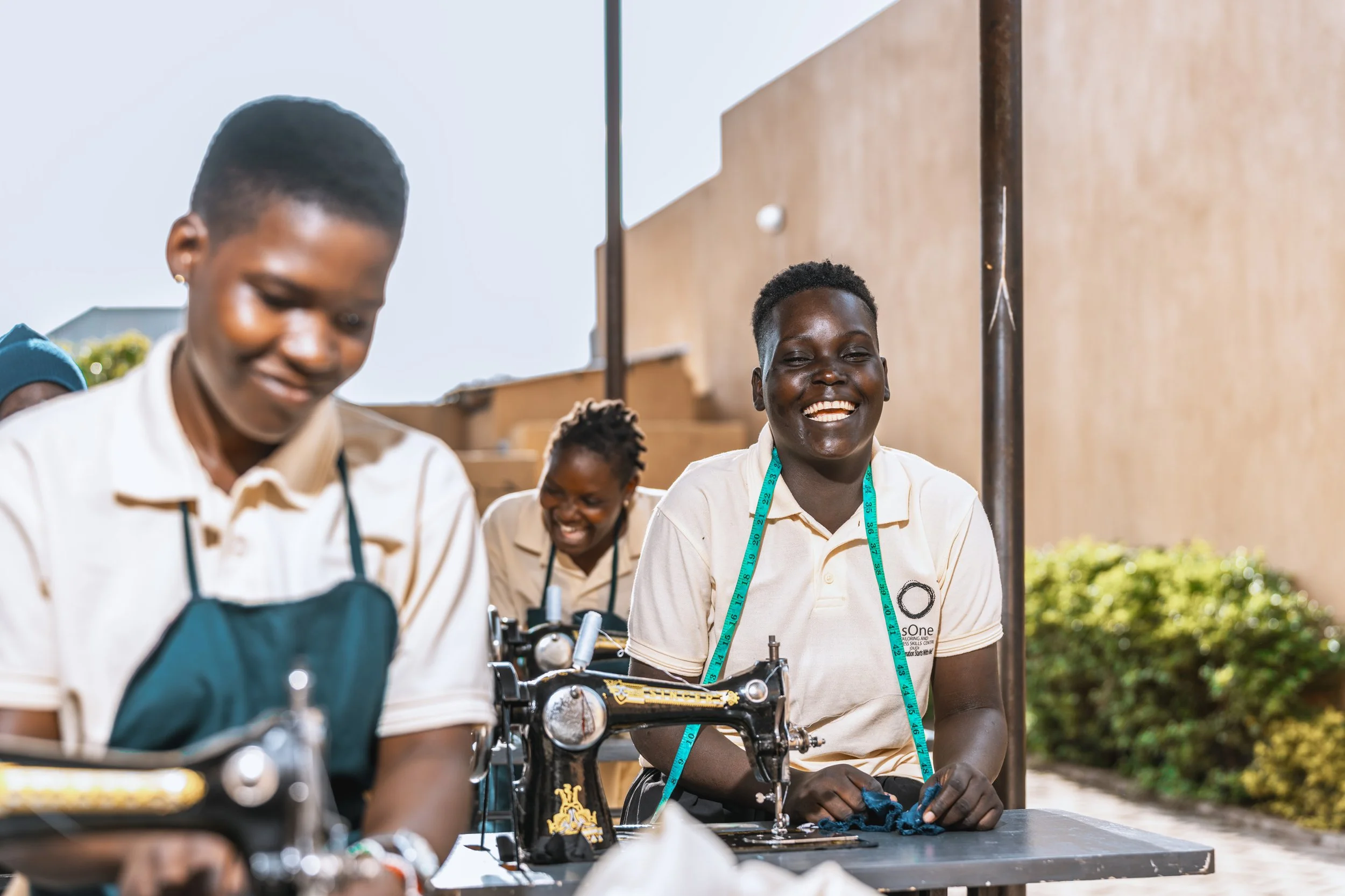 AsOne tailoring center students in Idudi smiling while sewing on machines
