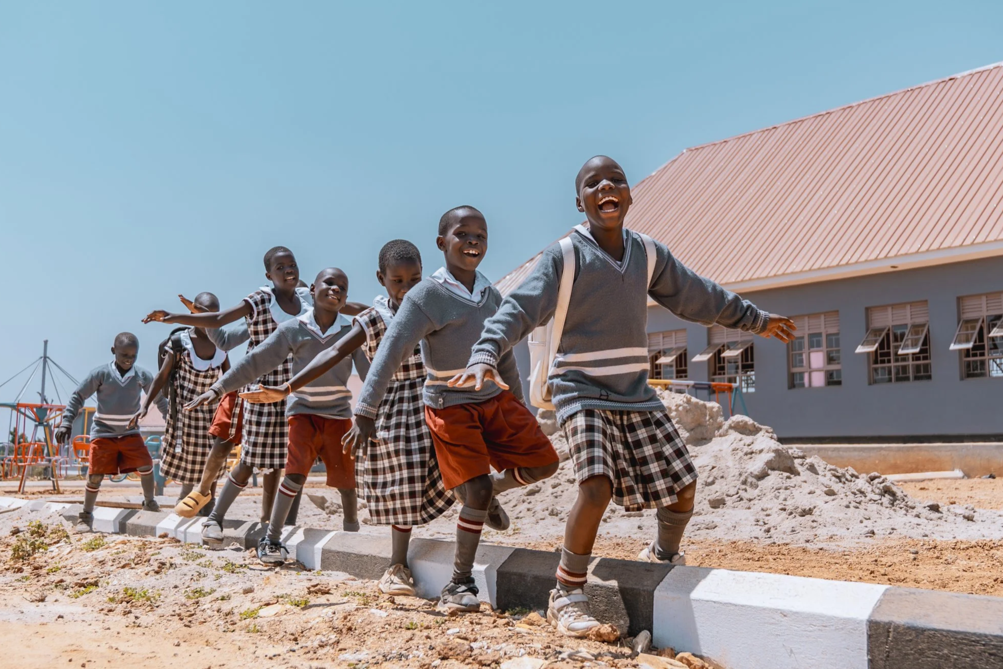 AsOne Nursery & Primary School, Serere students in uniform laughing and playing on curb steps outside their school