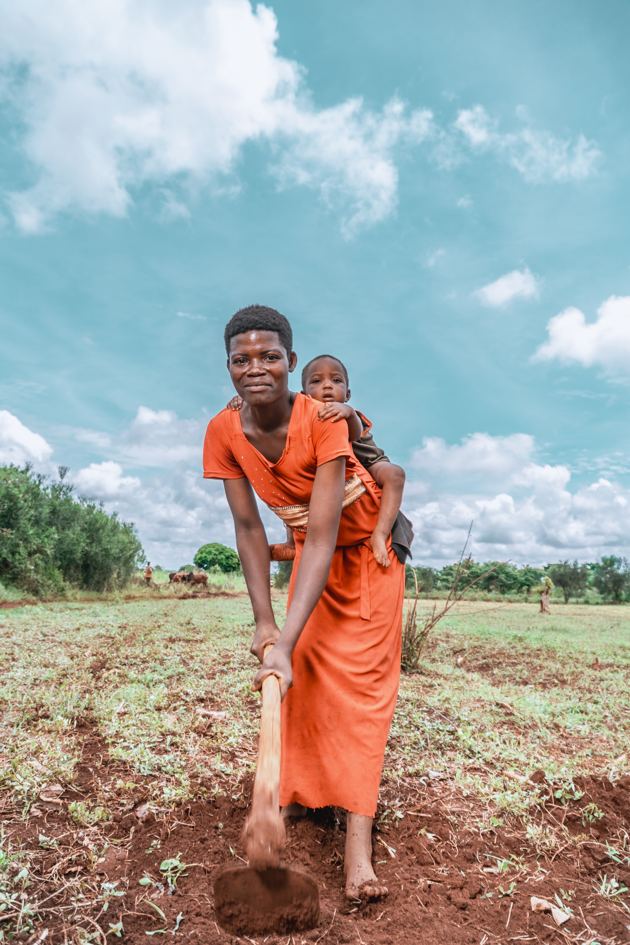AsOne agriculture program participant farming her field with her baby, Idudi, Uganda