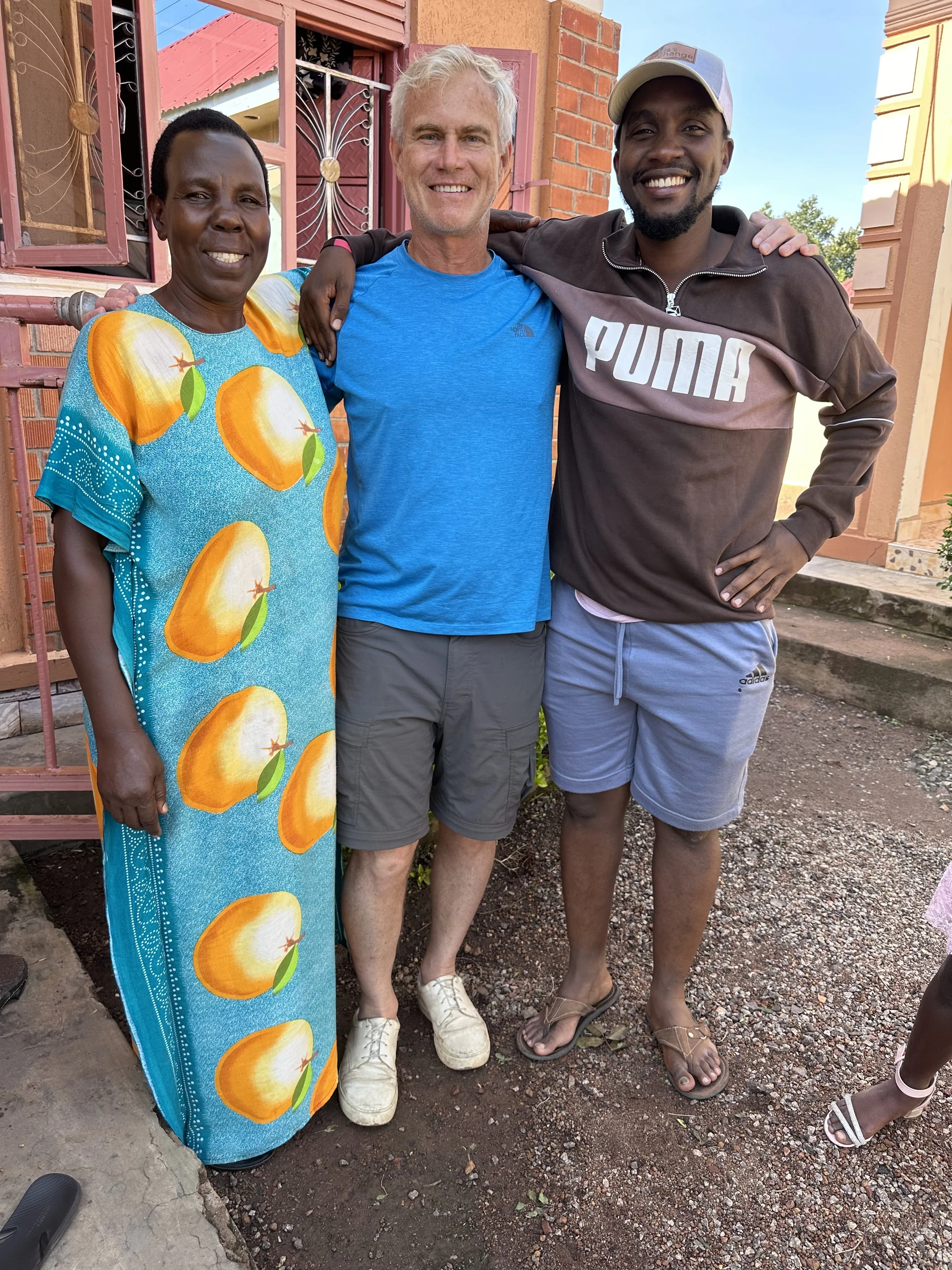 David, an AsOne donor, standing with two Ugandan community members outdoors