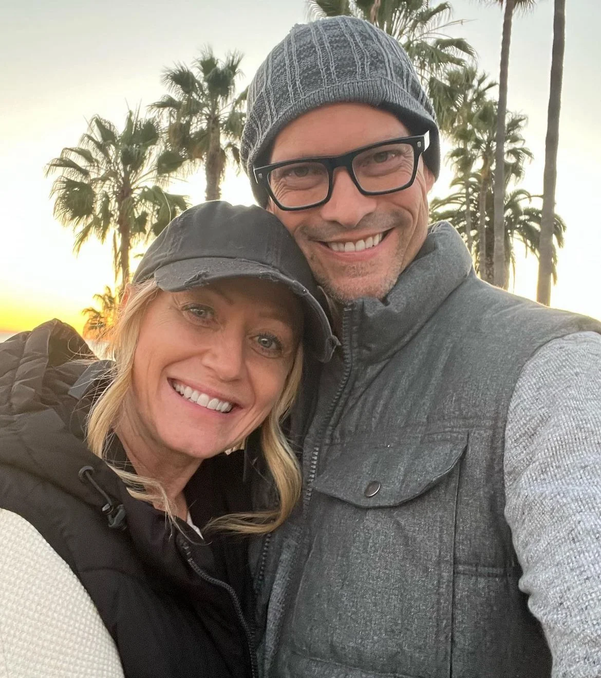 Chris and Jessica, AsOne donors, taking a selfie together with palm trees at sunset in the background