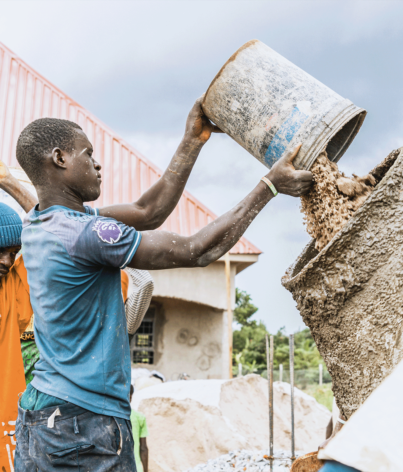 Construction worker pouring cement into a mixture at an AsOne school building site