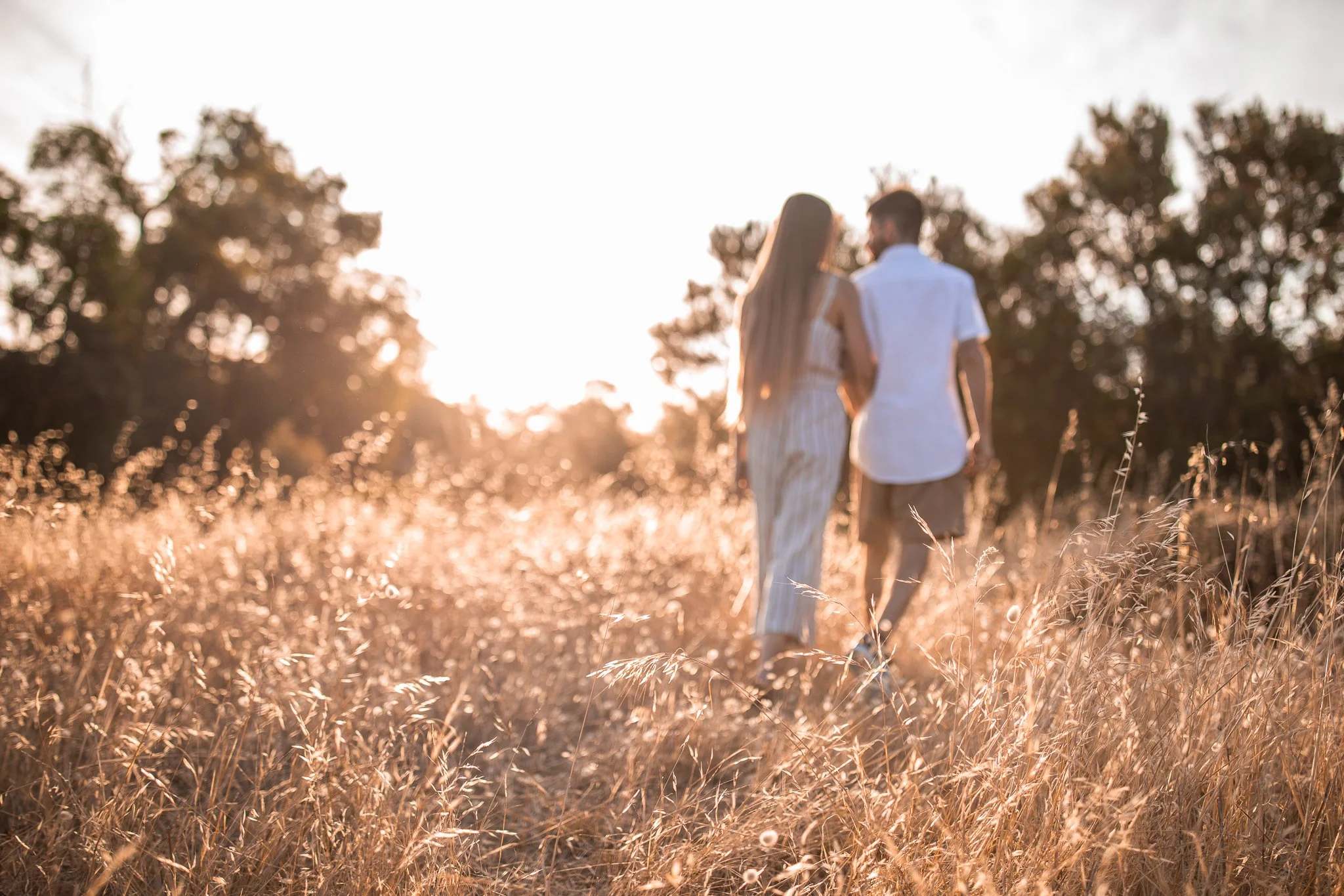 A couple holding hands walking through a grassy field at sunset.