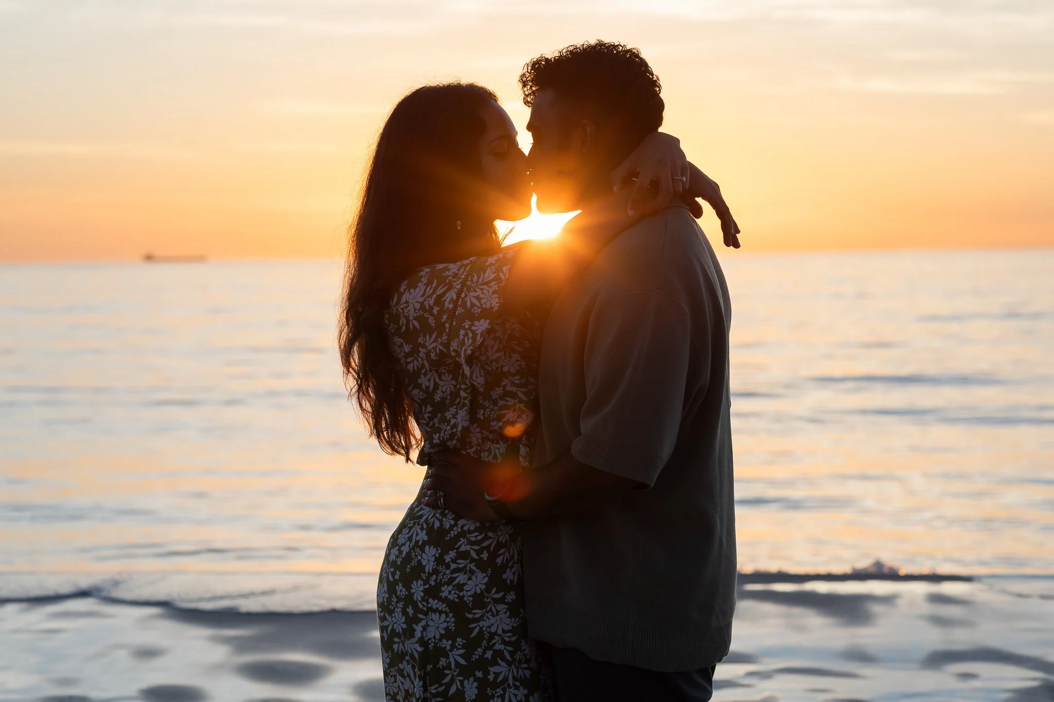Silhouetted couple kissing on the beach at sunset.