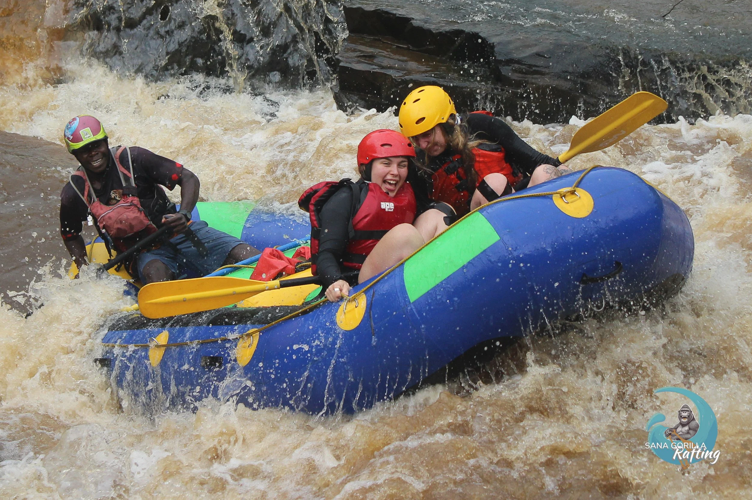 Three people rafting on River Birira in Uganda, wearing helmets and life jackets, navigating through whitewater rapids and smiling, having fun, full of adrenaline.