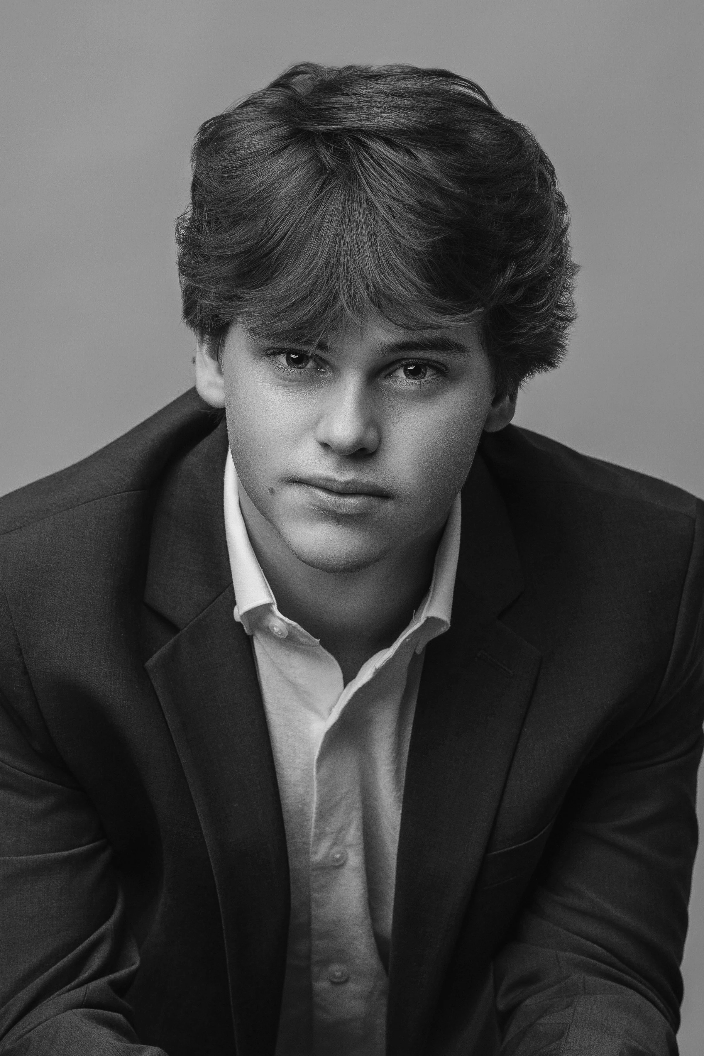 Modern senior portrait of a young man in a navy suit, posed against a gray studio backdrop. Captured by Sommer Ortiz Portraits in North Myrtle Beach, SC, specializing in classic and timeless senior photography for high school graduates.