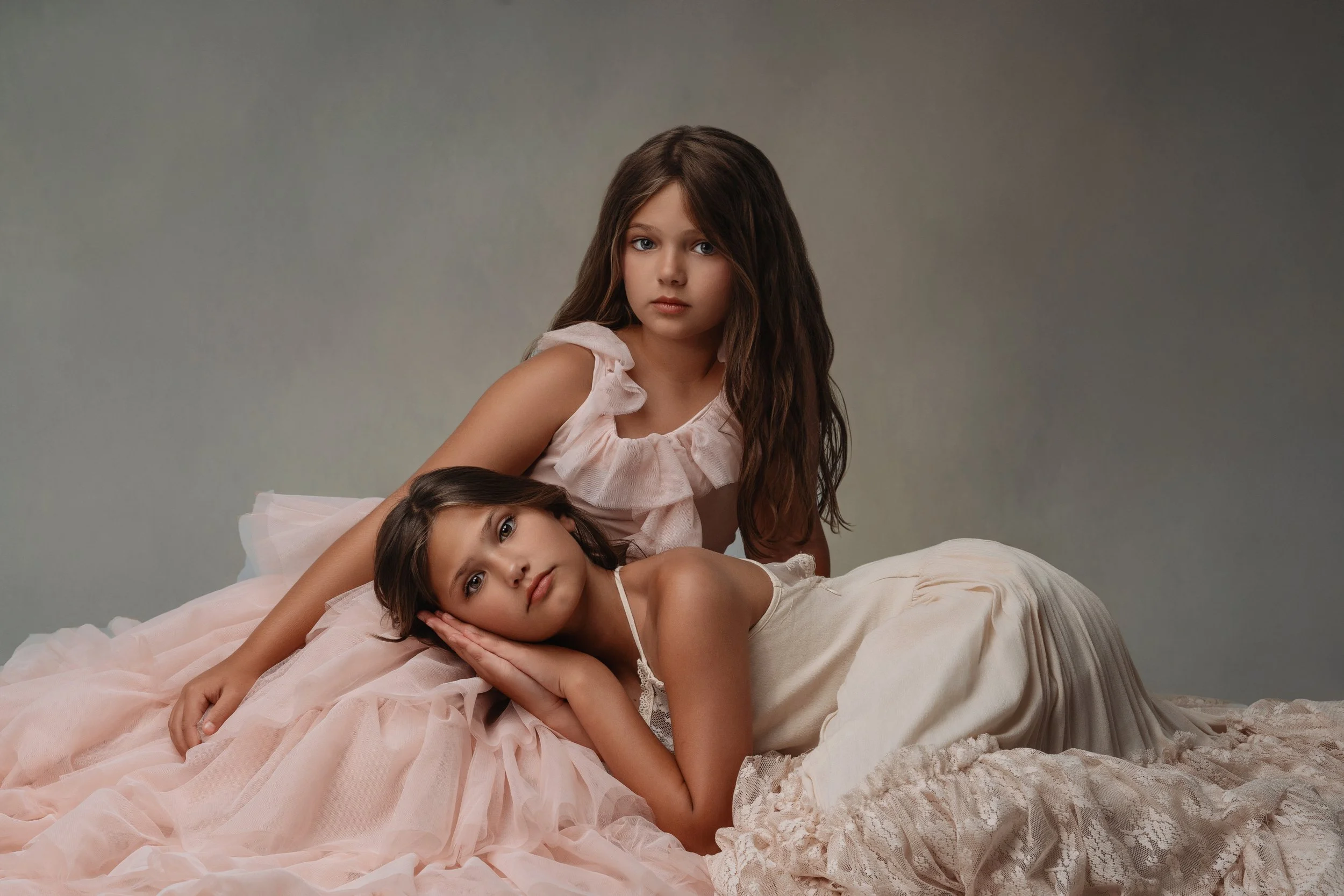 Dreamy portrait of two young sisters in elegant dresses, lying down ina serene setting. This image capture the calm and beauty of childhood, perfectly framed by Sommer Ortiz's expert photography. 