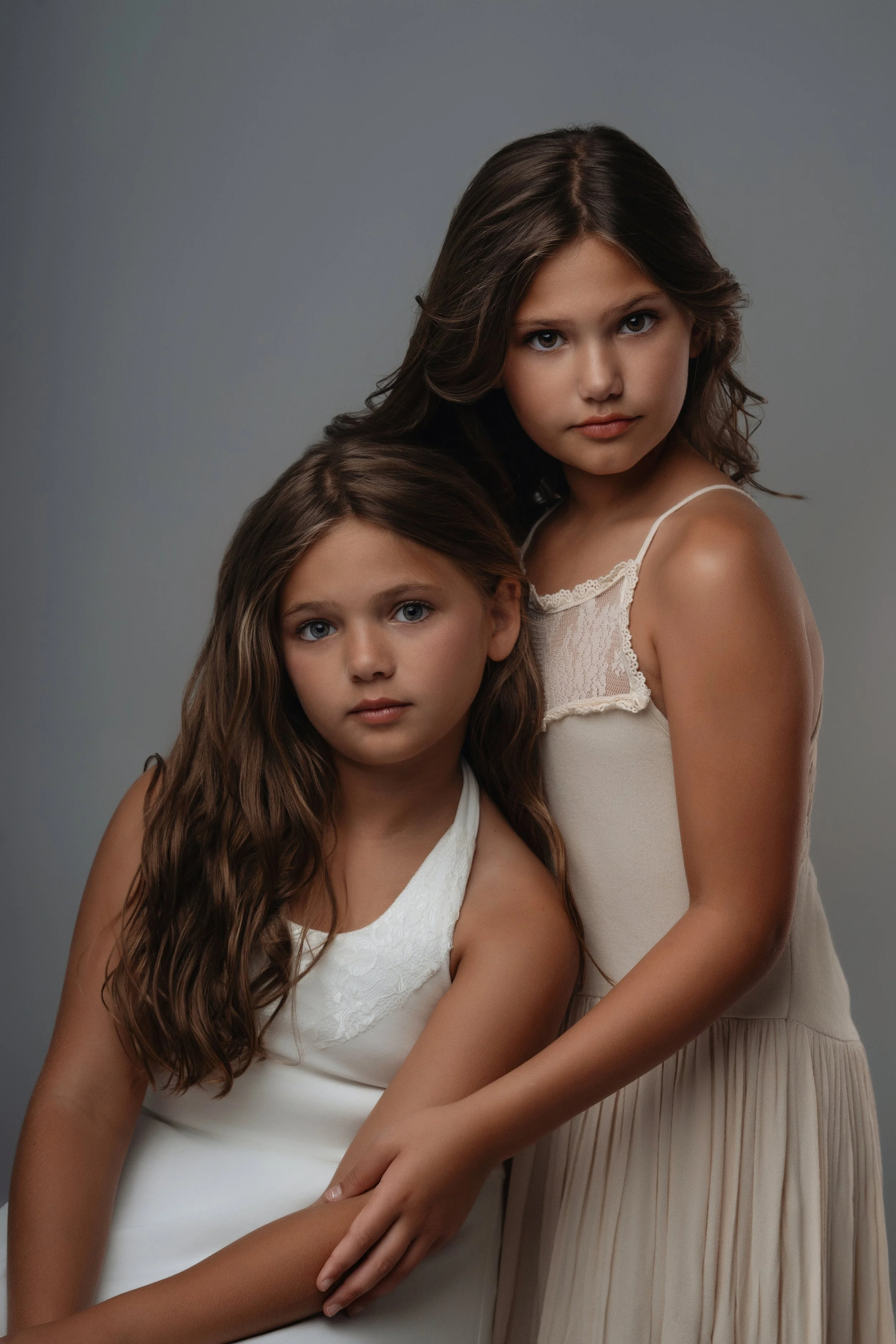 Beautiful studio portrait of two young sisters in elegant dresses. CApturing the bond and grace of sibling love, this portrait by Sommer Ortiz showcases exquisite lighting and composition.