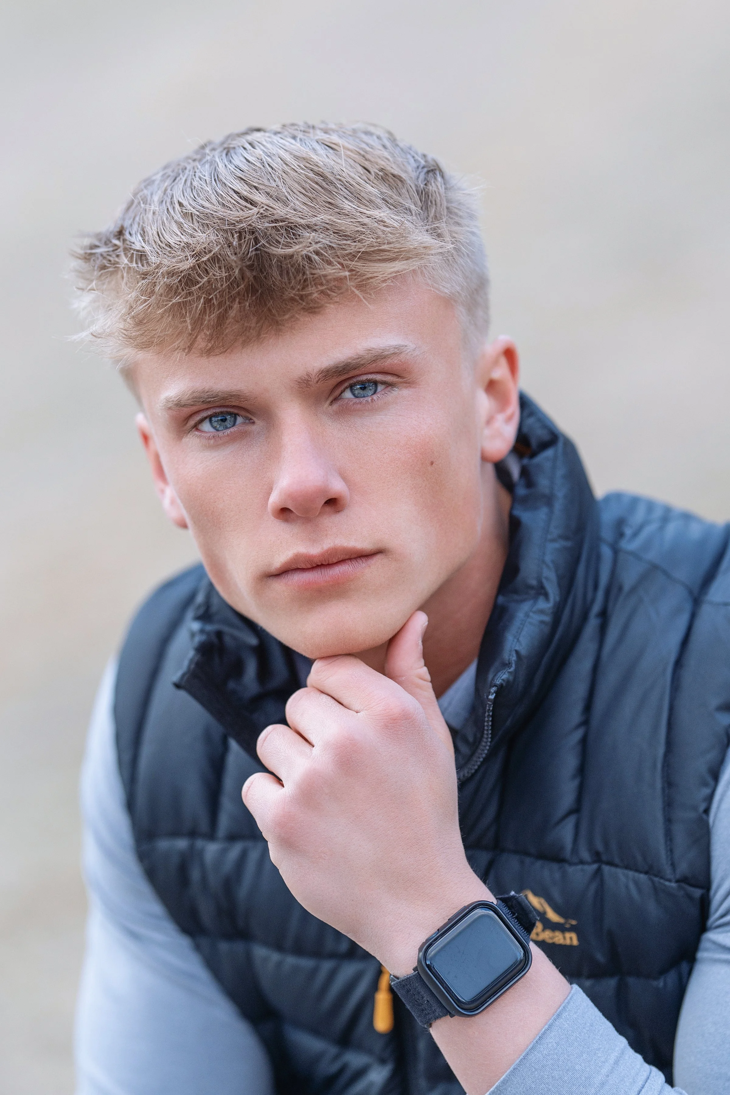 Stylish portrait of a young man in North Myrtle Beach, thoughtfully posing with a black vest and smartwatch, exemplifying a blend of casual and tech savvy elegance. Ideal for lifestyle and fashion editorial photography.