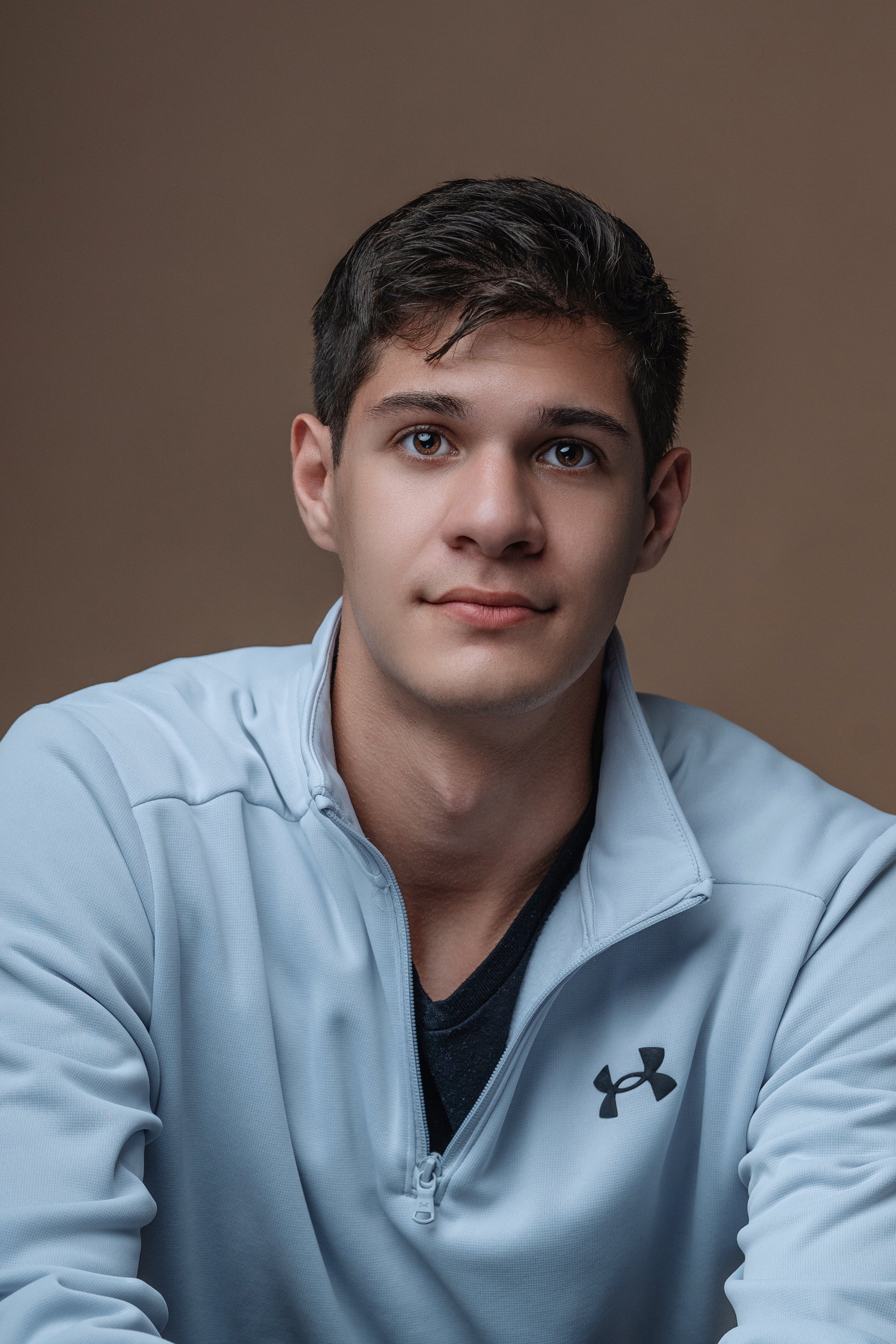 Engaging portrait of a high school senior guy in Myrtle Beach, wearing a light blue Under Armour jacket, with a relaxed yet confident expression. The neutral background accentuates his features, making it an excellent example of High school senior ph