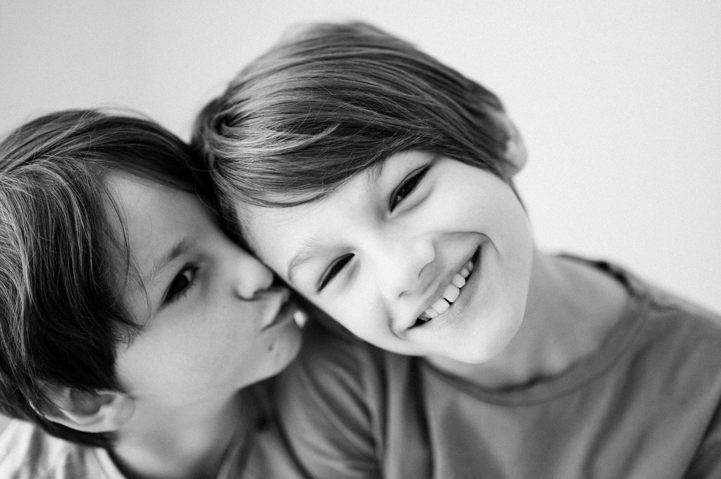 Due bambini sorridenti con i capelli corti e scuri si abbracciano, la scena è in bianco e nero.
