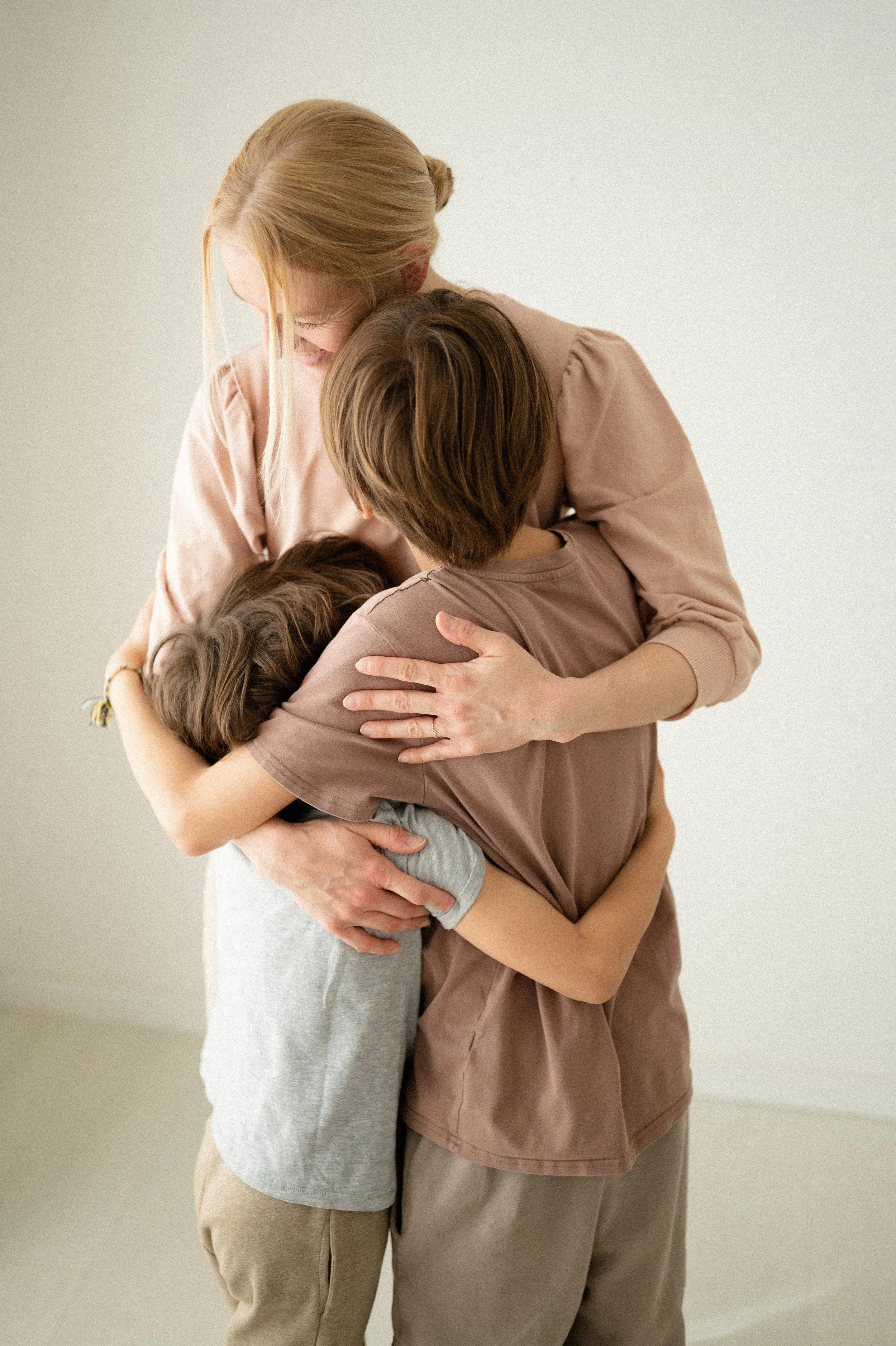 Una donna e due bambini stanno abbracciandosi felicemente in una stanza con pareti chiare.