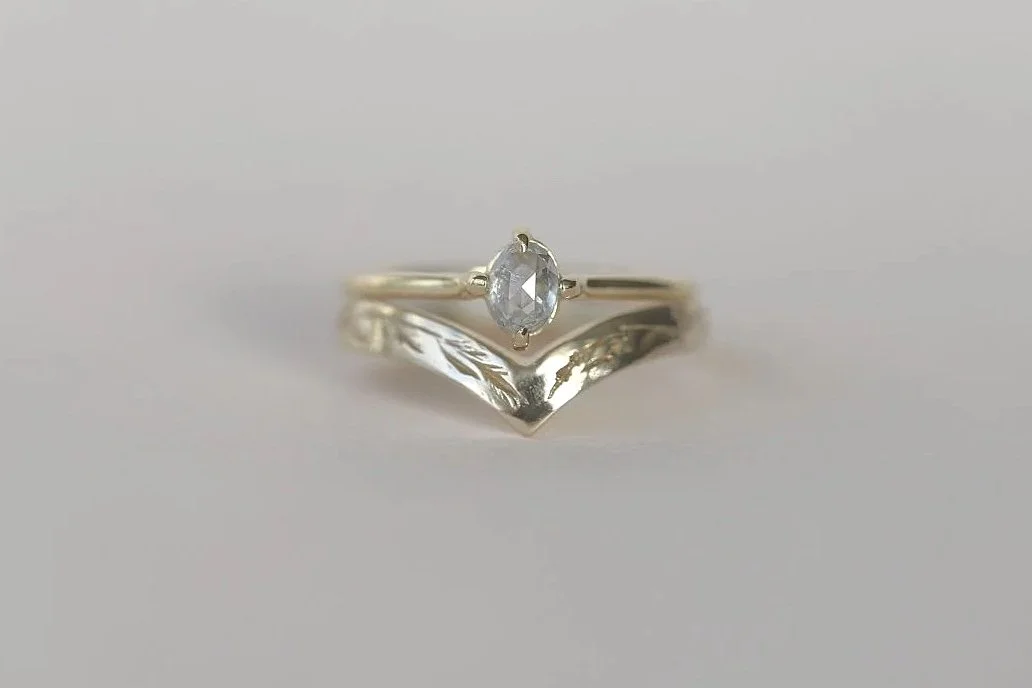 A silver ring with an oval-shaped clear gemstone in a prong setting, with a V-shaped decorative band underneath.