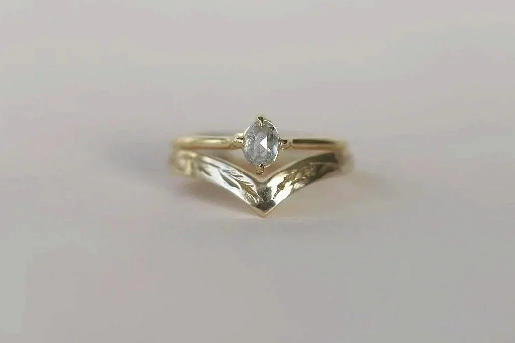 A silver ring with an oval-shaped clear gemstone in a prong setting, with a V-shaped decorative band underneath.