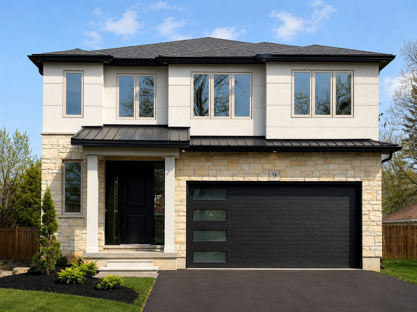 Modern two-story house with a black garage door, stone accents, and trees reflected in large windows during daytime.