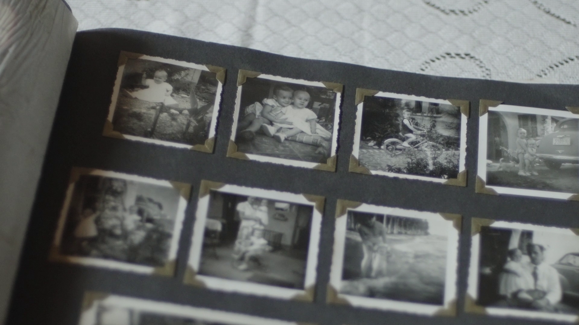 A collection of black and white vintage photographs displayed in a photo album, with some photos showing children playing, riding bikes, and outside scenes.