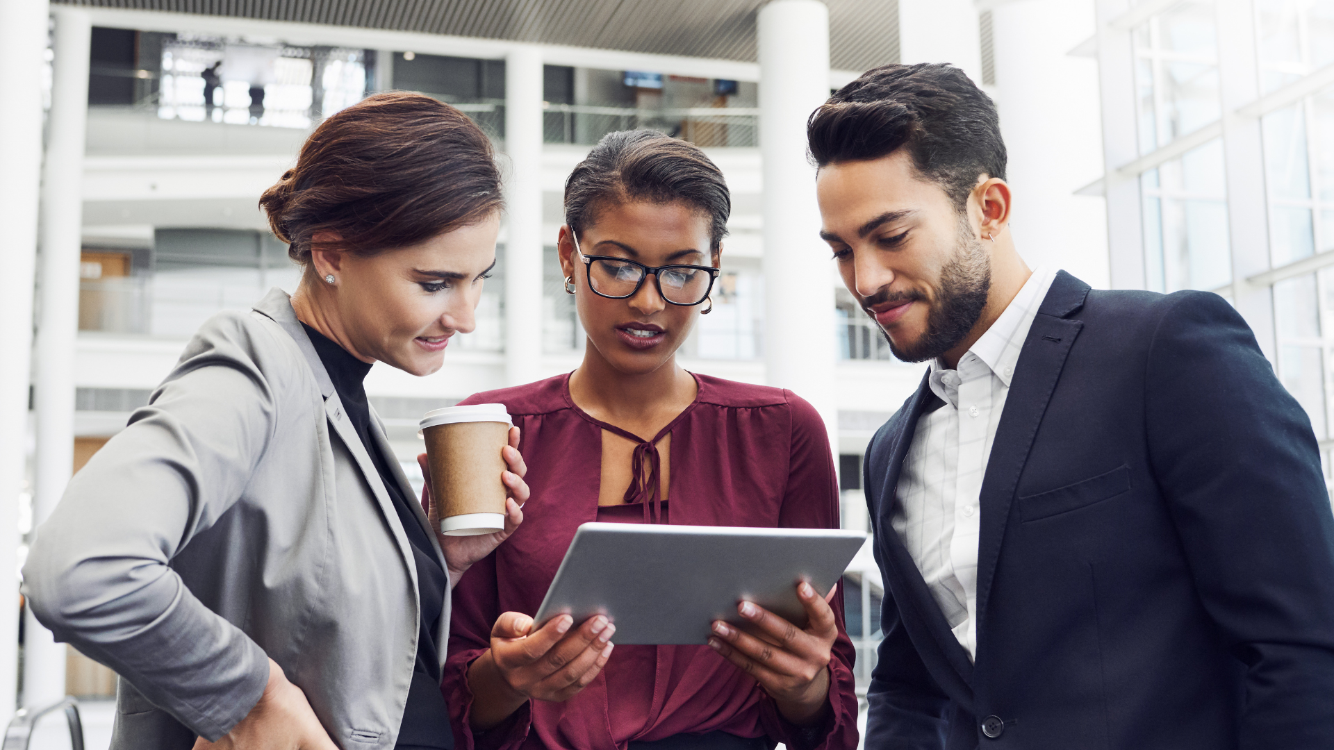 Three diverse professionals in a corporate environment reviewing a project on an iPad, illustrating sponsorship and career progression for underrepresented talent.