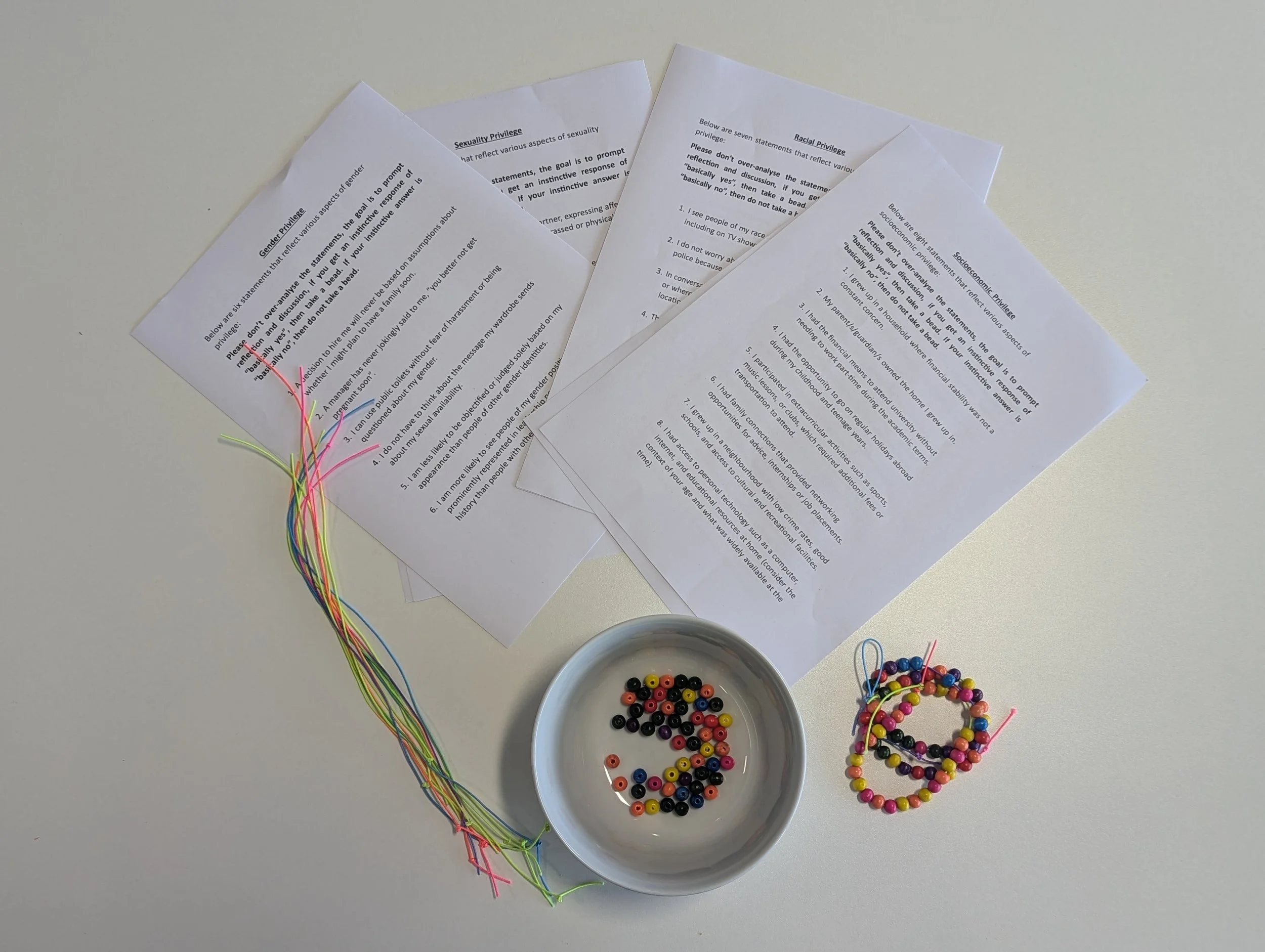 Creative workshop activity exploring identity, privilege and belonging through collaborative bracelet making, each bead added to participant's thread is acquired because they have said yes to a statement, the statements link to areas of privilege.