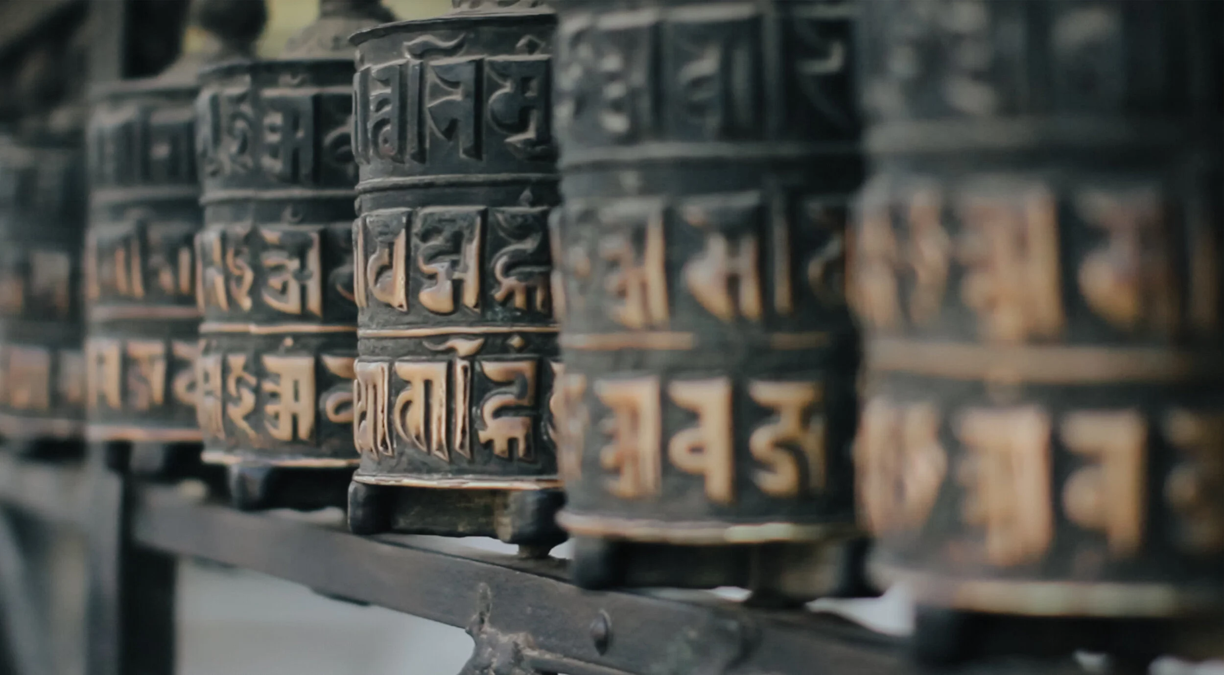 Close-up of several rows of metal prayer wheels with engraved Sanskrit characters, mounted on a horizontal axle.