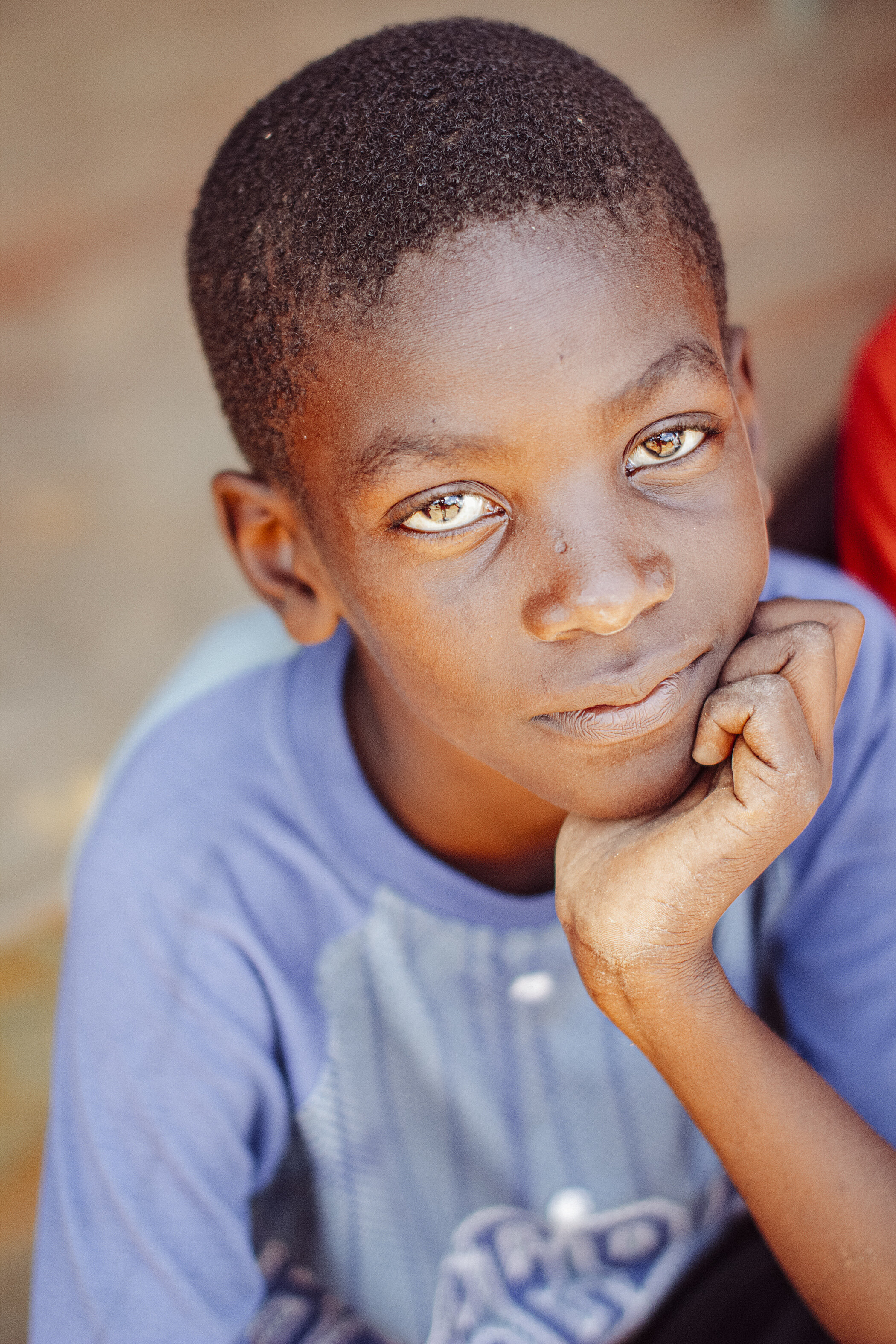 Close-up of a young boy with short hair resting his chin on his hand, looking directly at the camera.
