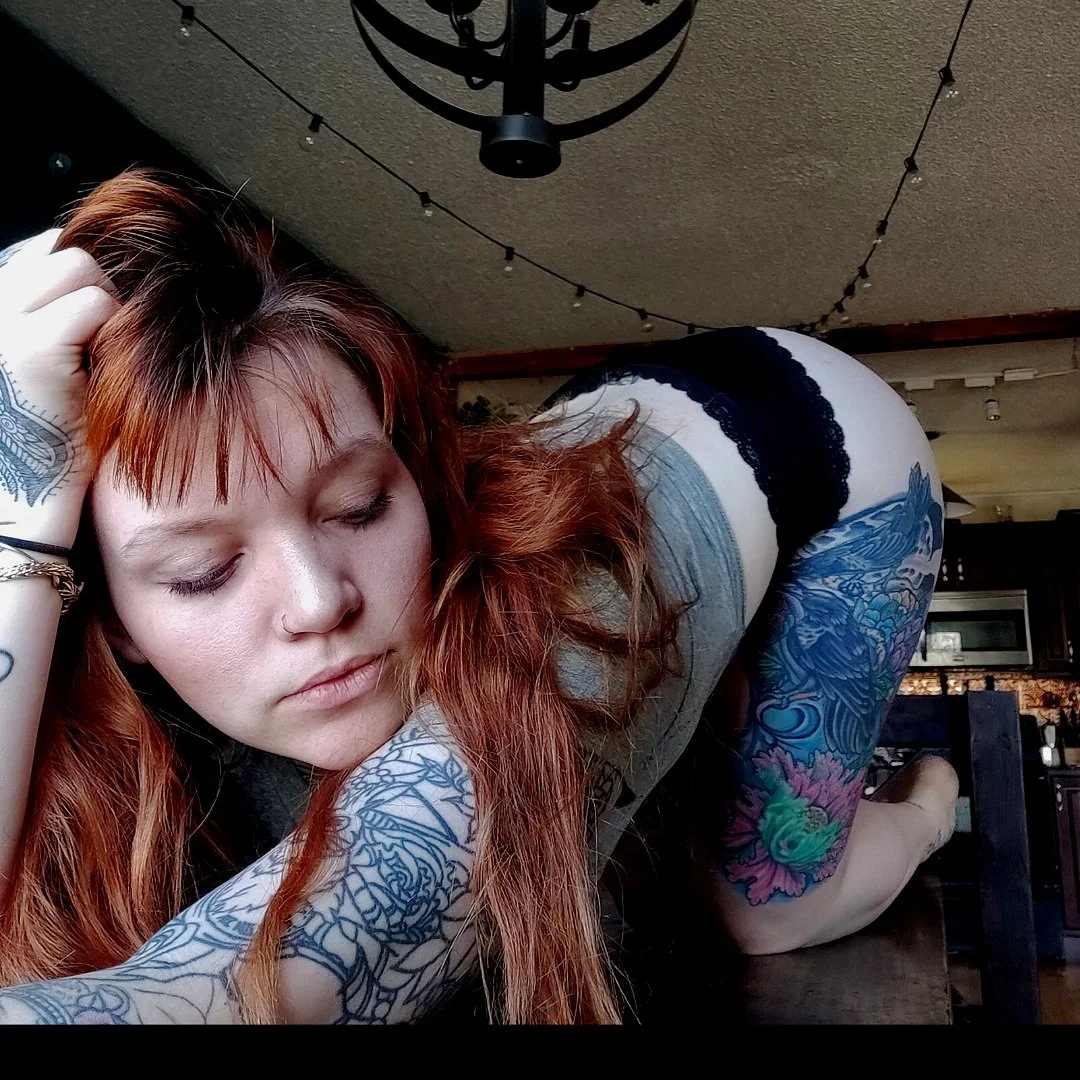 A person with tattoos on their arms and legs lying on a table, framed by a chandelier and string lights.