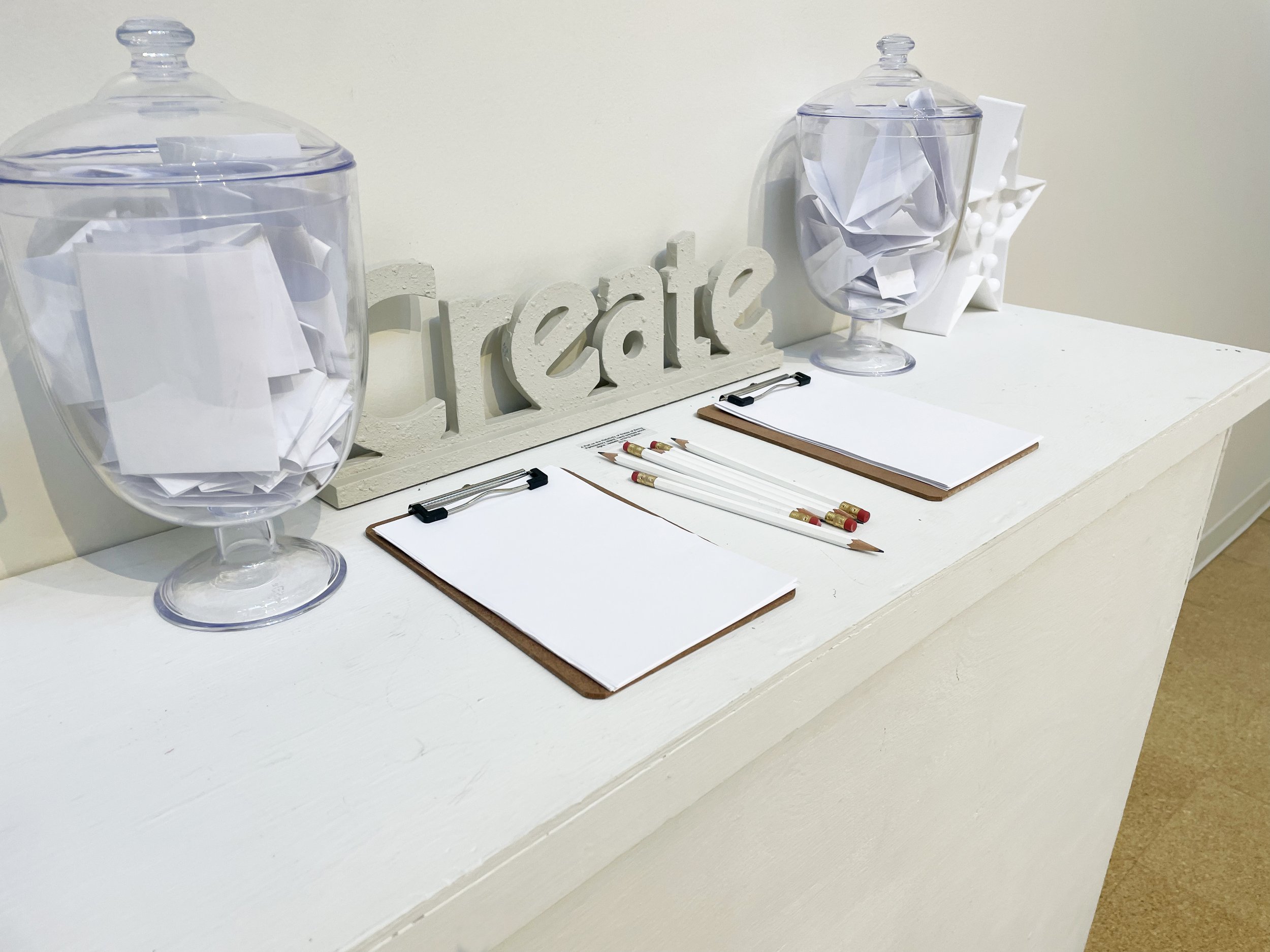"What is Comfort? / What is Suffering?" 2016-present. Participatory Installation (wood signs, inspirational decor, plastic vessels, clipboards, pencils). Dimensions variable.