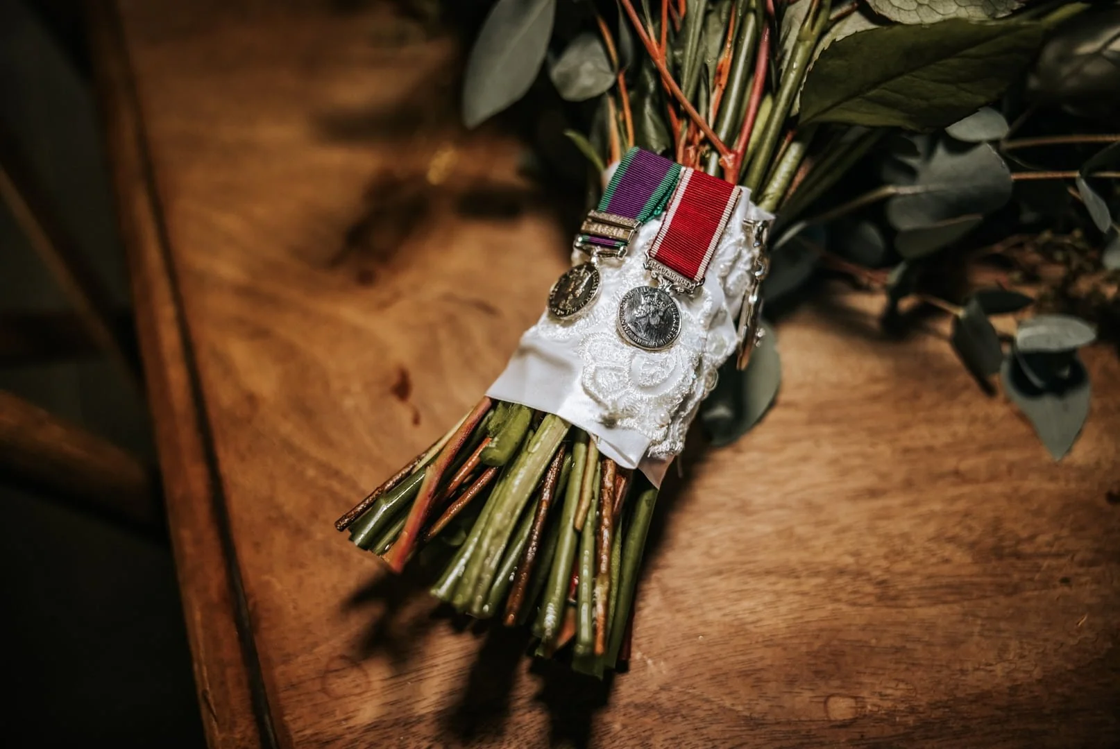 Wedding bouquet handle wrapped in lace from the bride’s mother’s wedding dress, with military medals and a locket of forget-me-nots as sentimental tributes to family.
