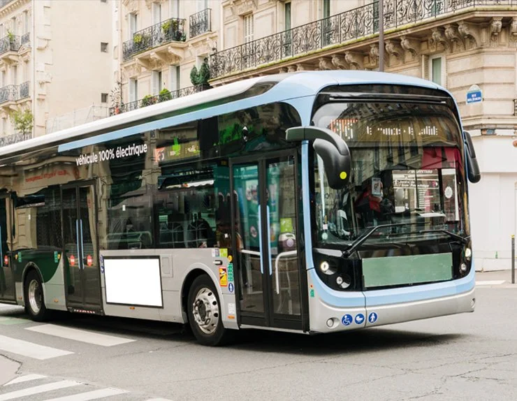 A modern electric bus driving on a city street in Paris, France, with apartment buildings in the background.