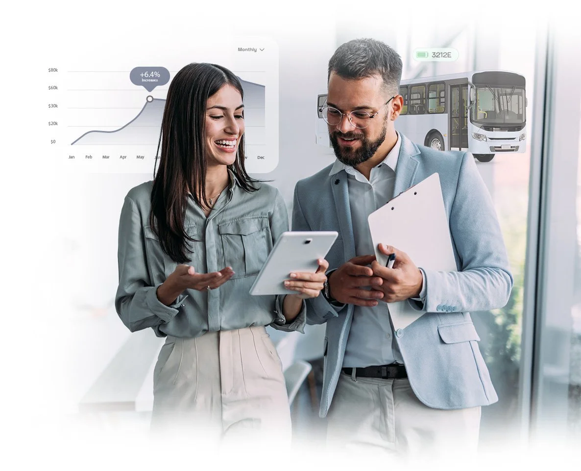 Two professionals, a woman and a man, discussing while looking at a tablet in an office with graphs and a bus diagram in the background.