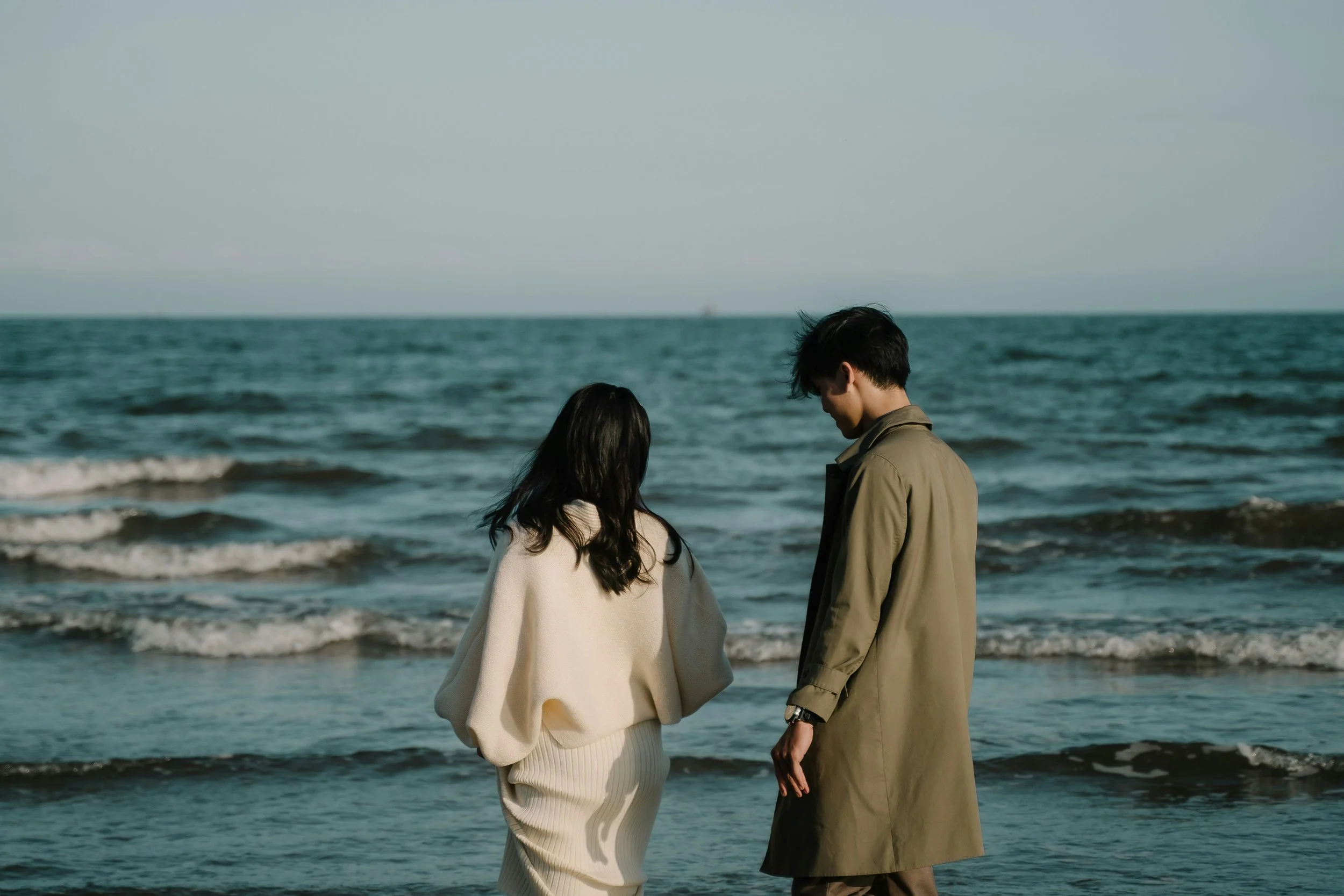 a man and a woman standing on a beach next to the ocean