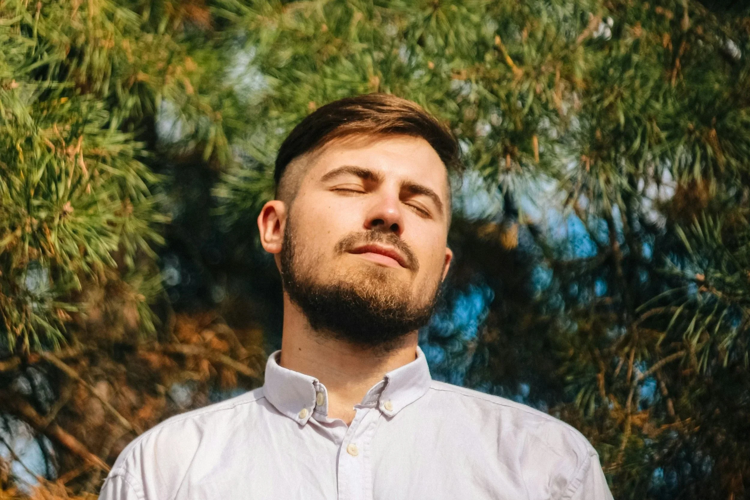 man in white dress shirt standing near green trees during daytime